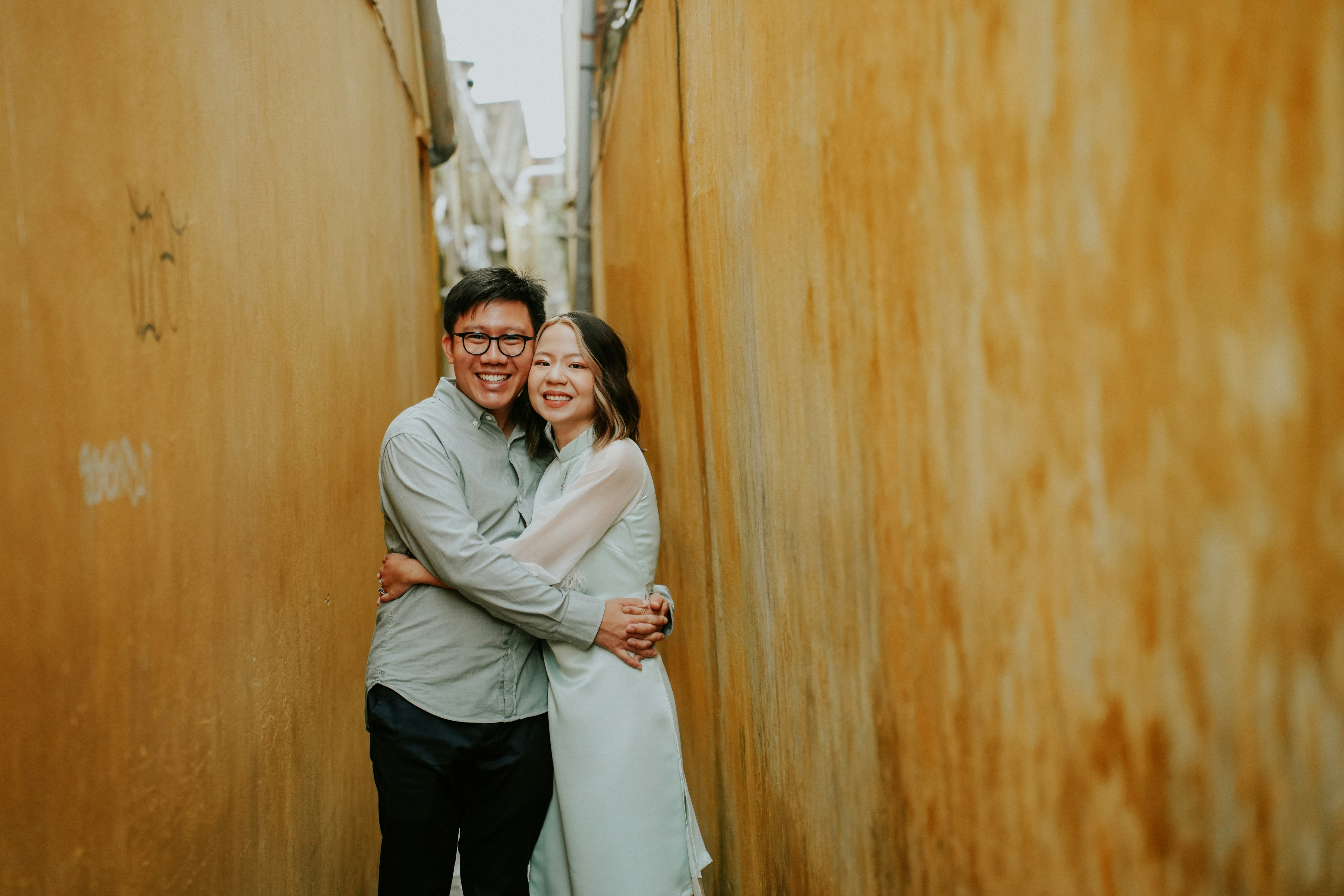 A couple embraces in a narrow, textured alleyway.