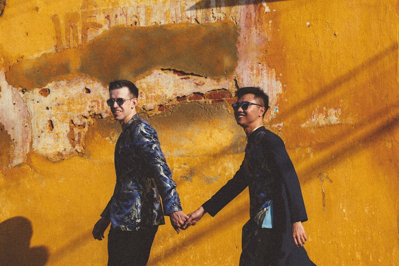 Two men holding hands in front of yellow wall