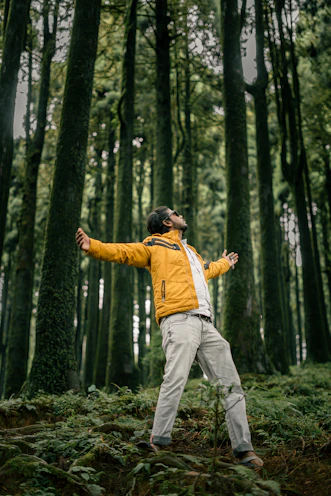 Man with arms outstretched in a lush green forest.