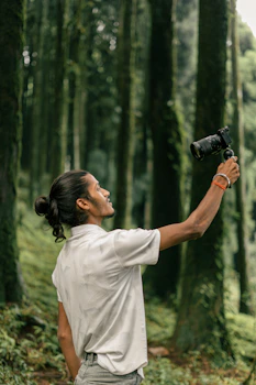 Man holding camera in a lush green forest.