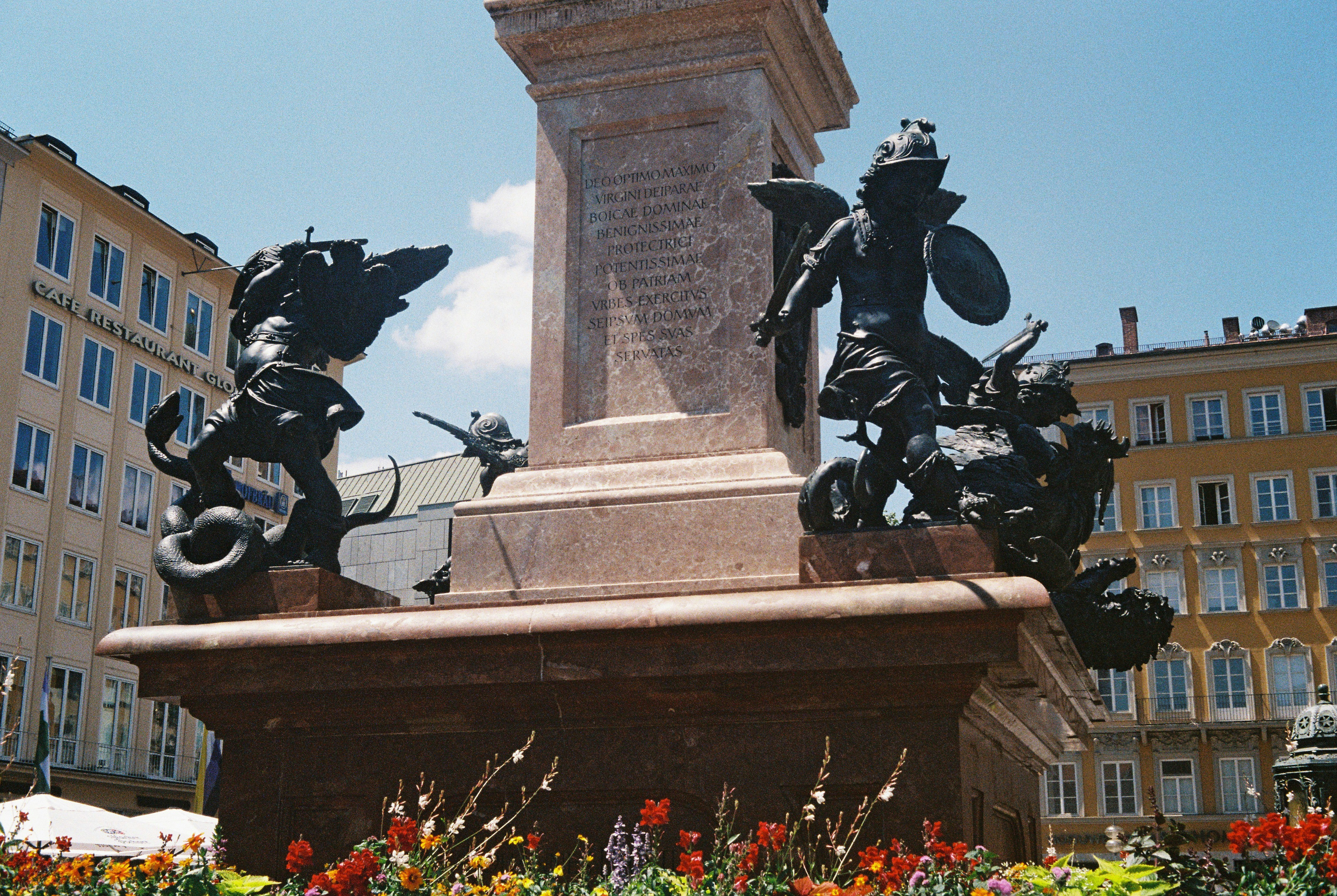 Monument with bronze sculptures and flowers in foreground.