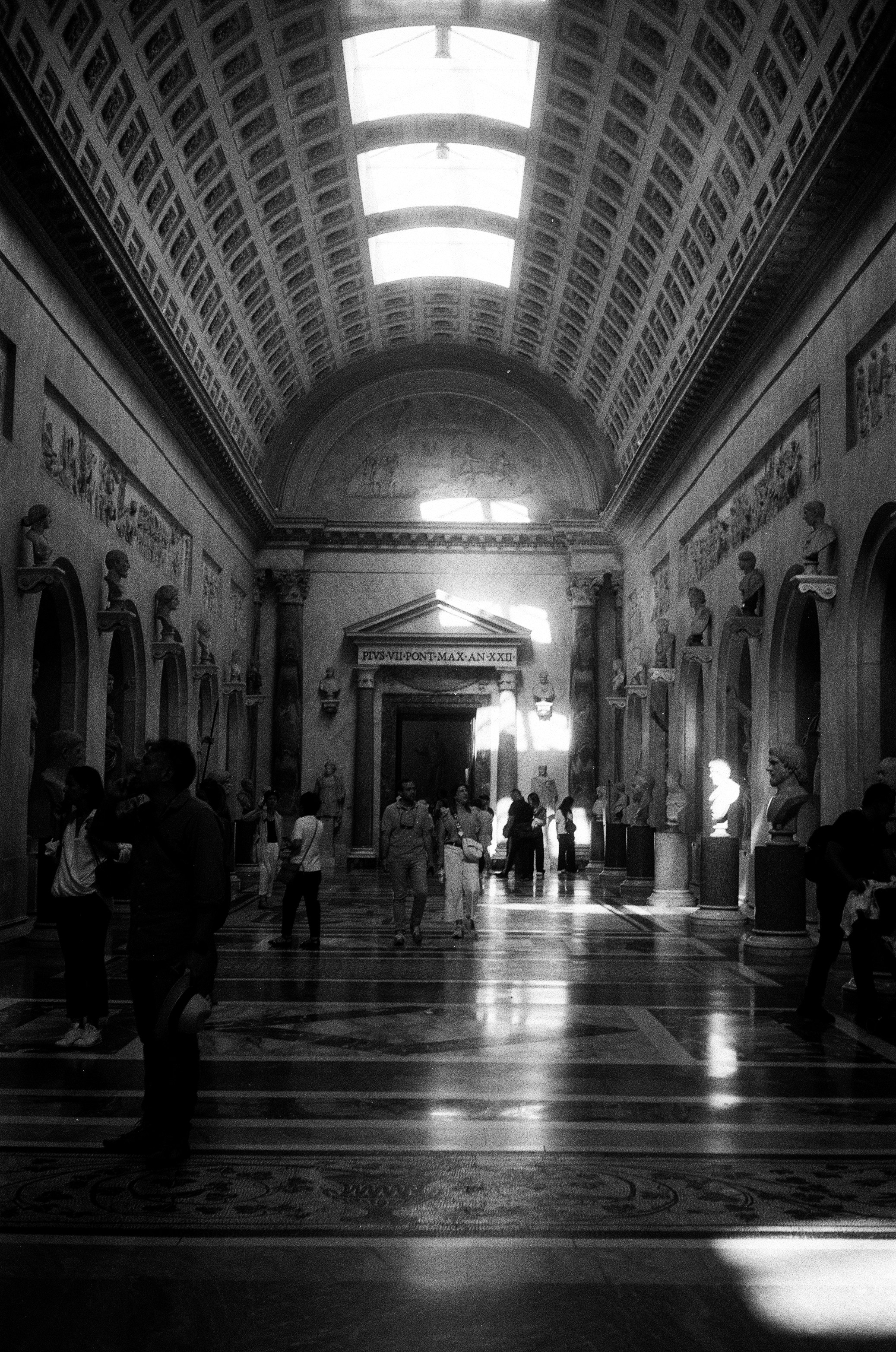 People walk through a grand, sunlit museum hall.