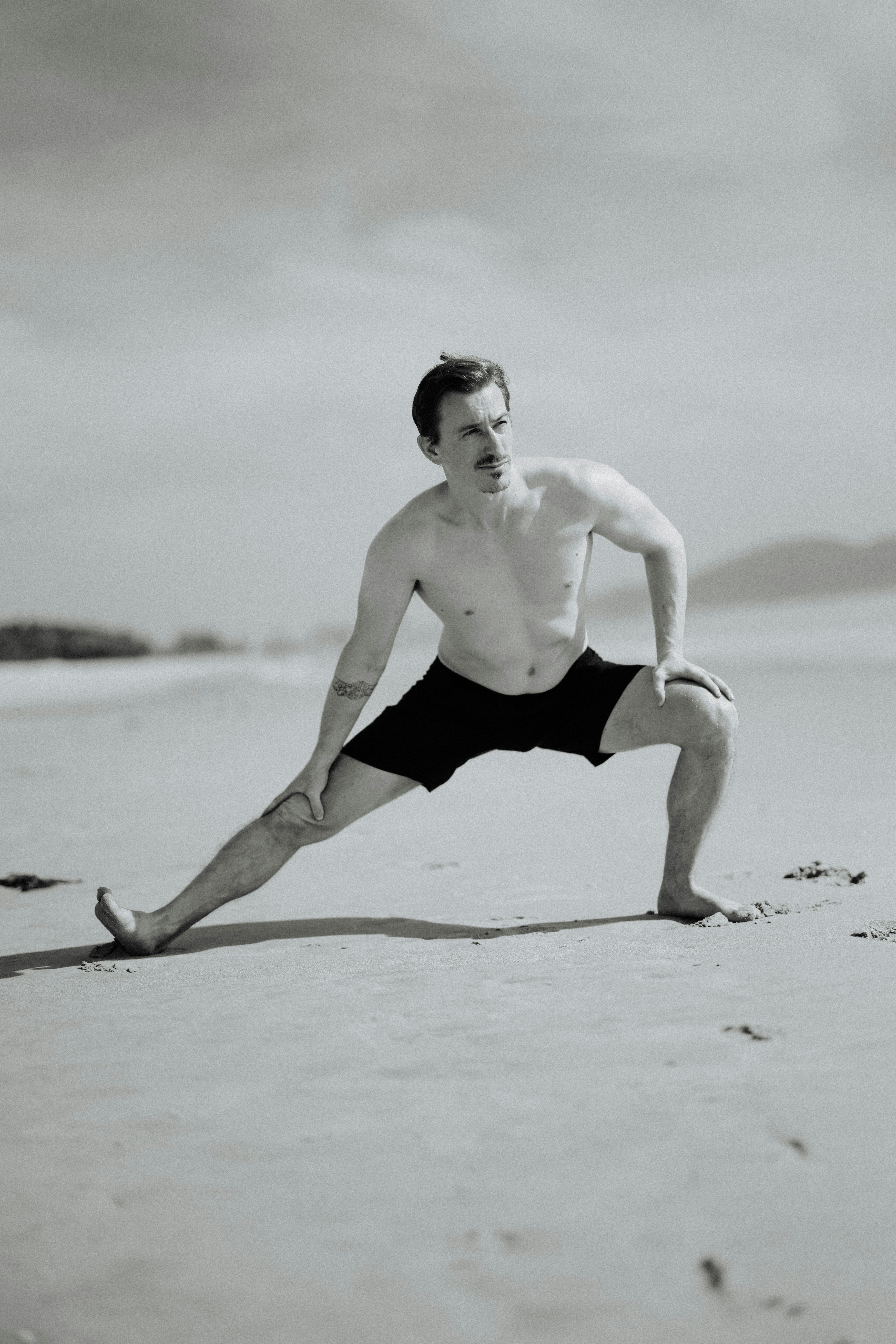 Man stretching on a sandy beach during the day.