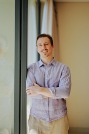 A smiling man leaning against a window