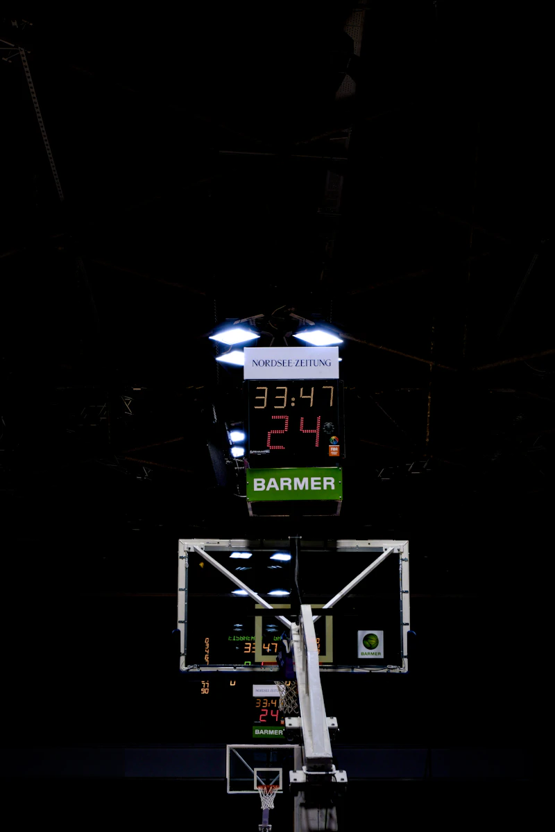 Illuminated basketball scoreboard above a hoop in a dark gym