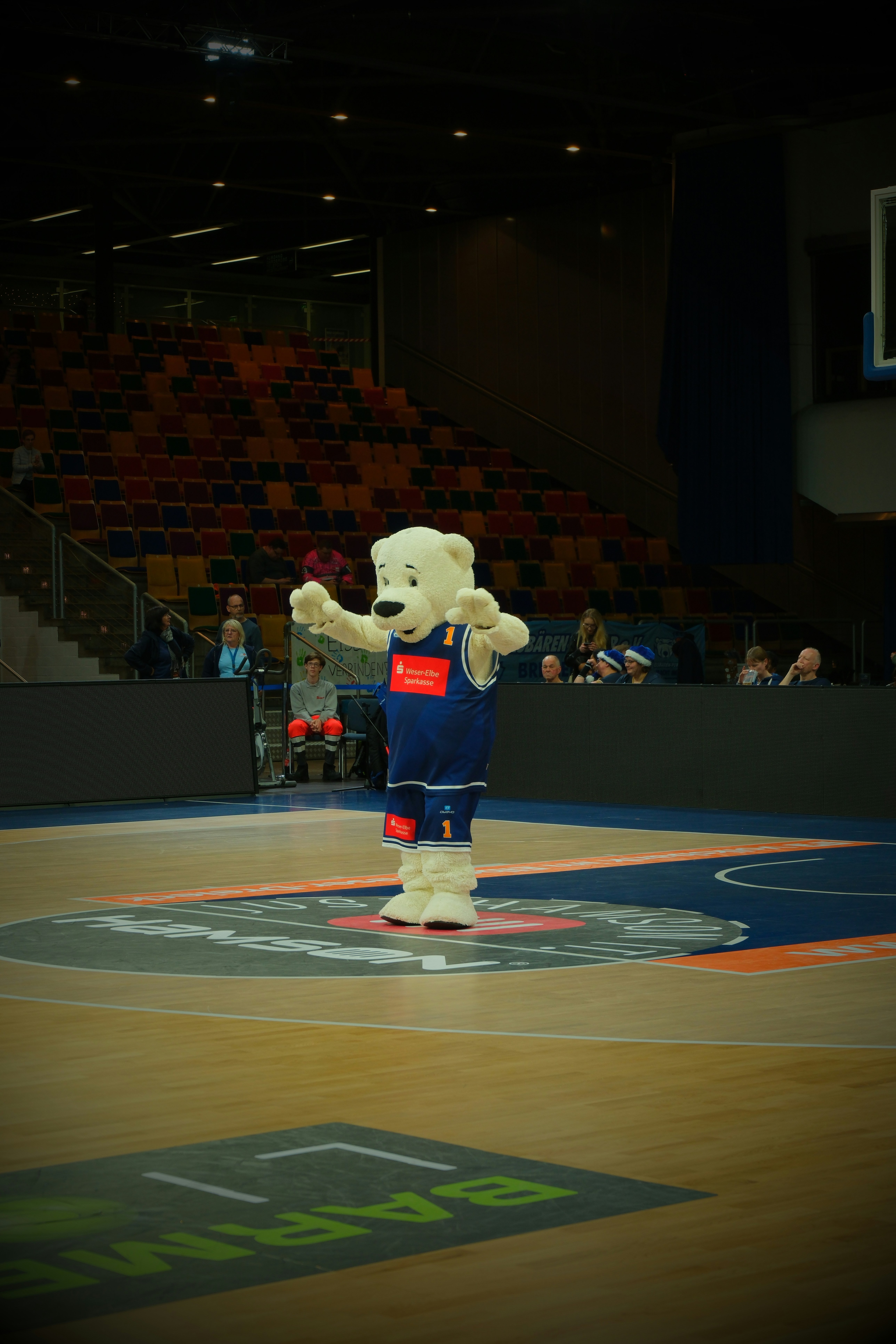 A polar bear mascot in a blue basketball jersey on a court