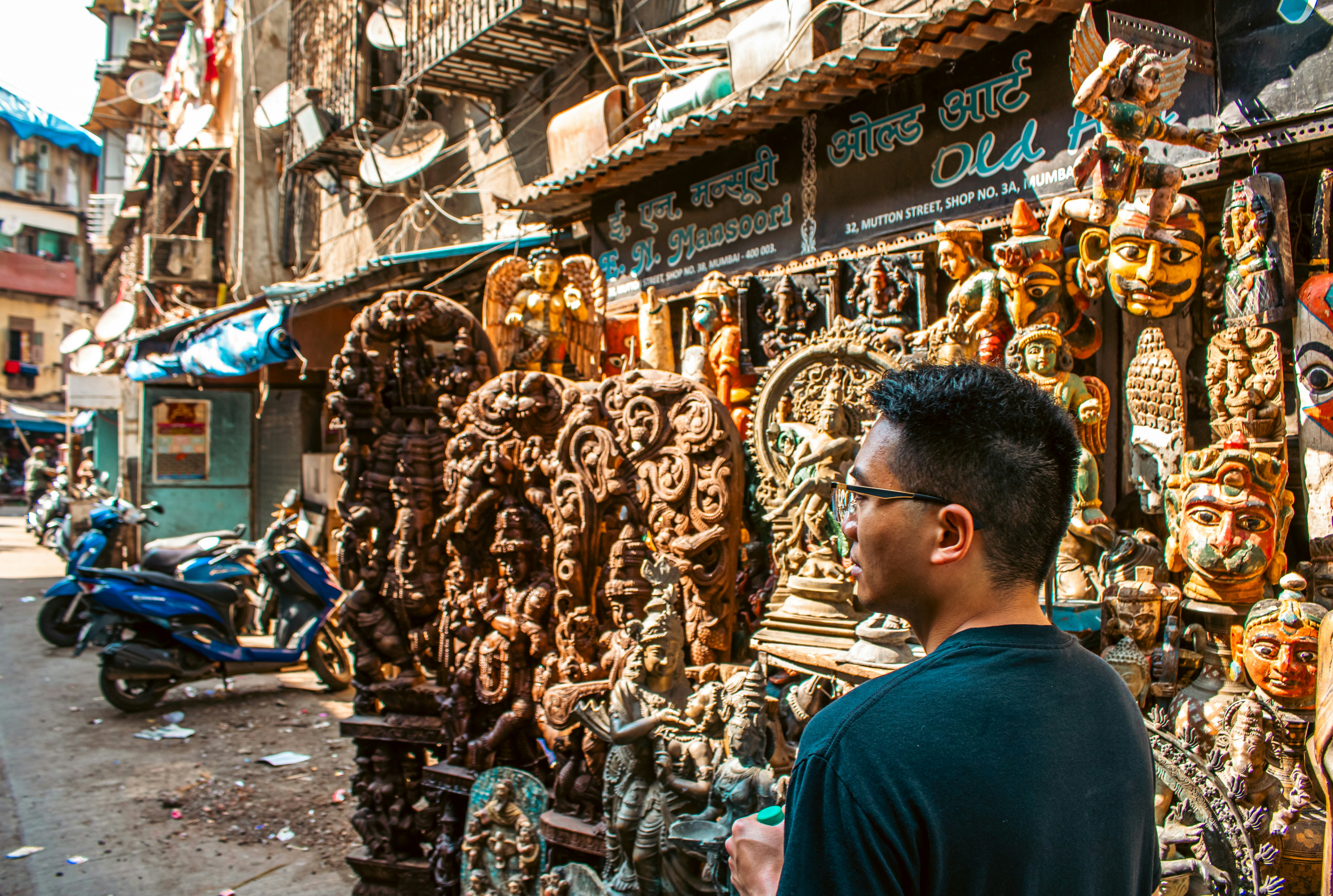 Man looks at carved wooden masks and statues displayed outside.