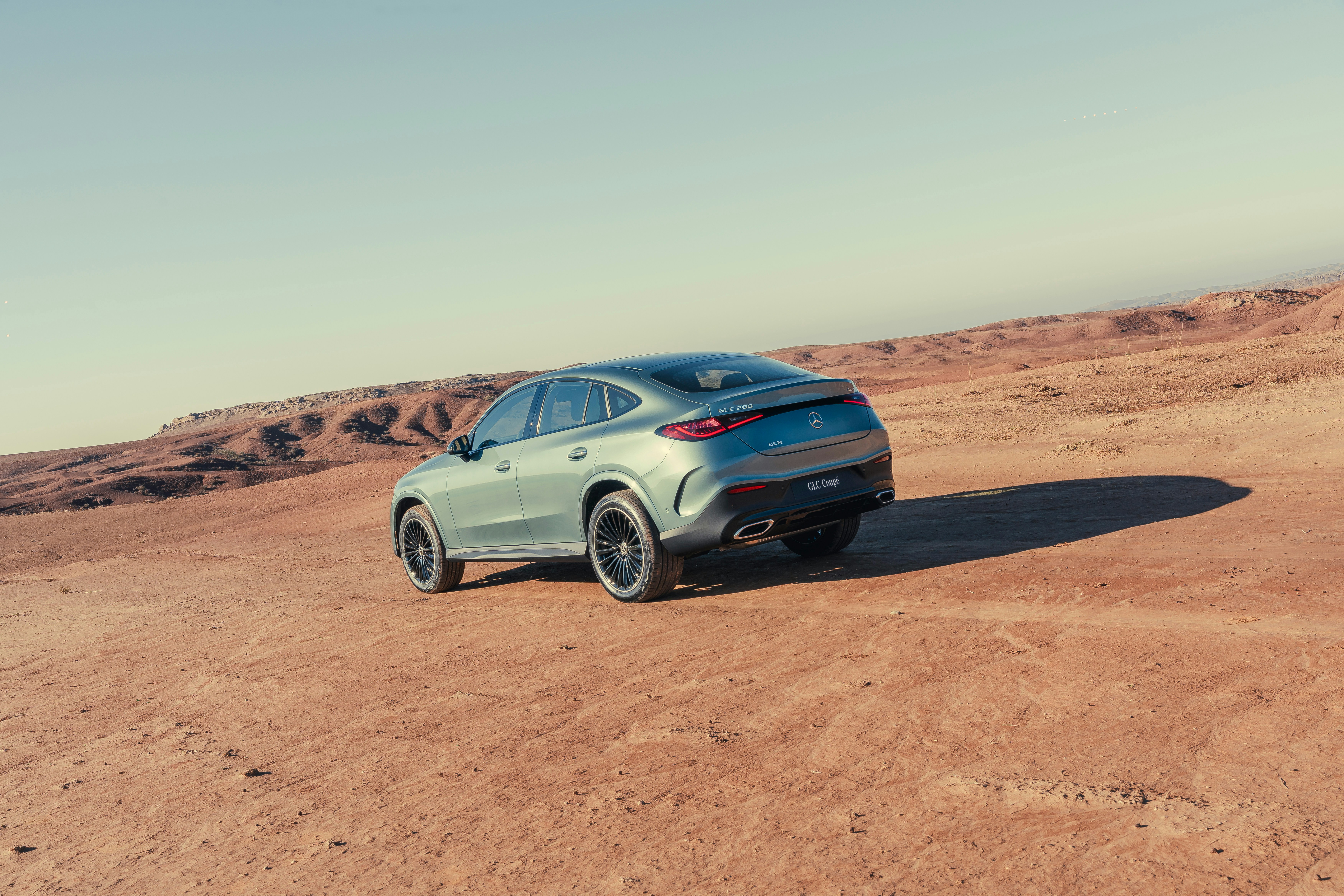 A light green suv parked on a dusty, arid landscape.
