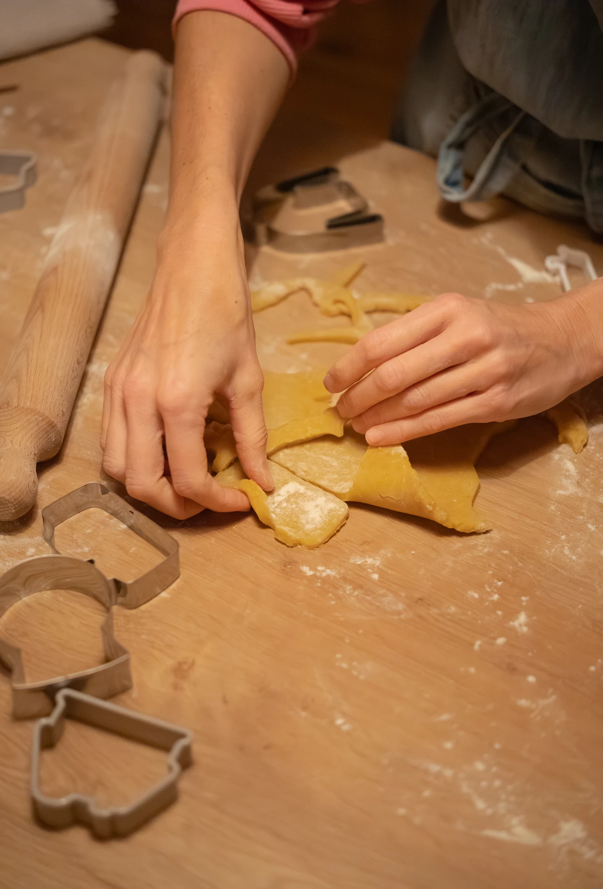Hands cutting dough with cookie cutters and rolling pin