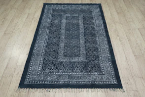 A dark patterned rug with fringe on wooden floor