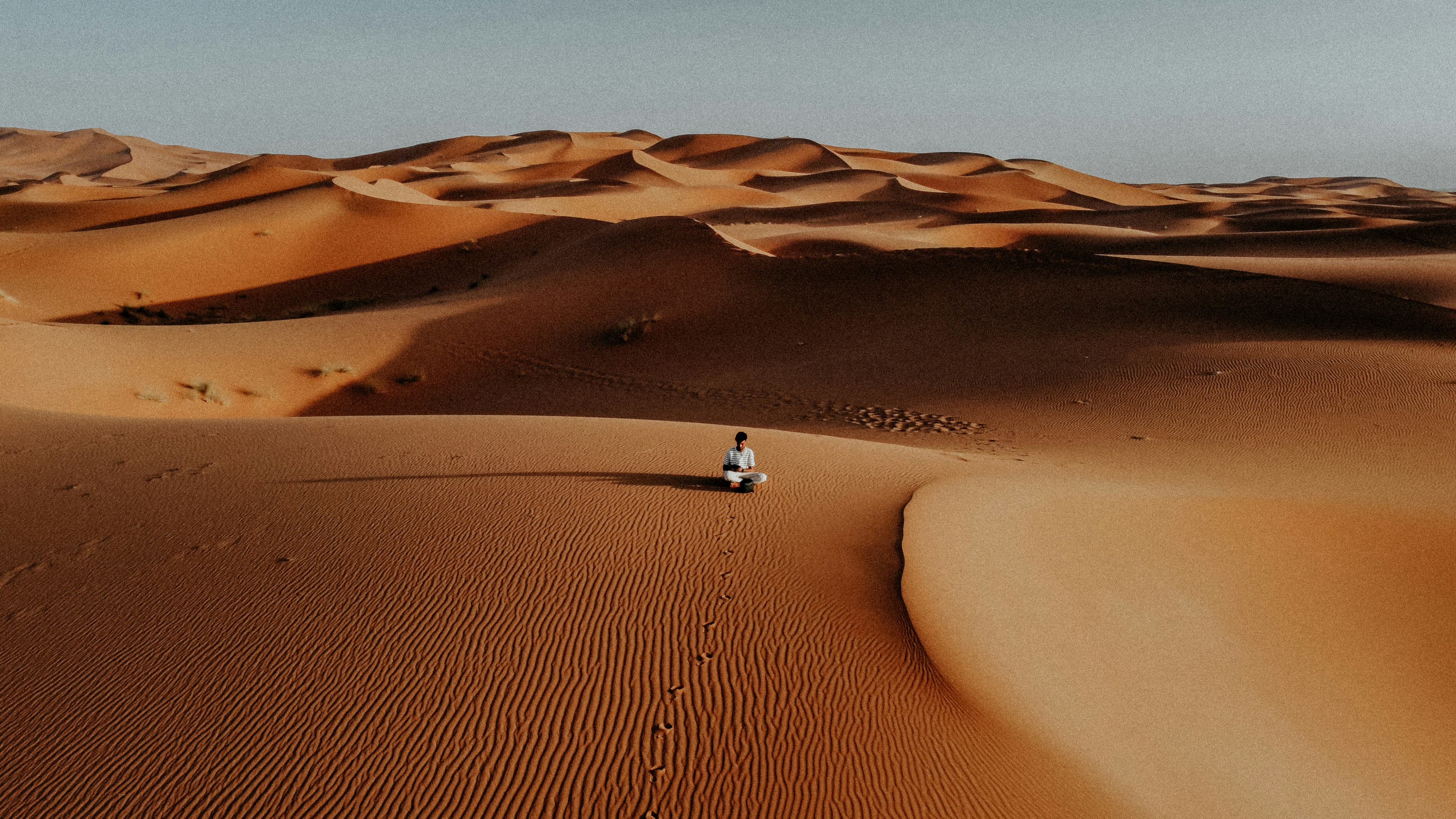 A lone figure walks across vast desert sand dunes.