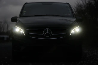A dark mercedes van with its headlights on.