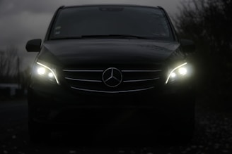 A dark mercedes van with its headlights on.