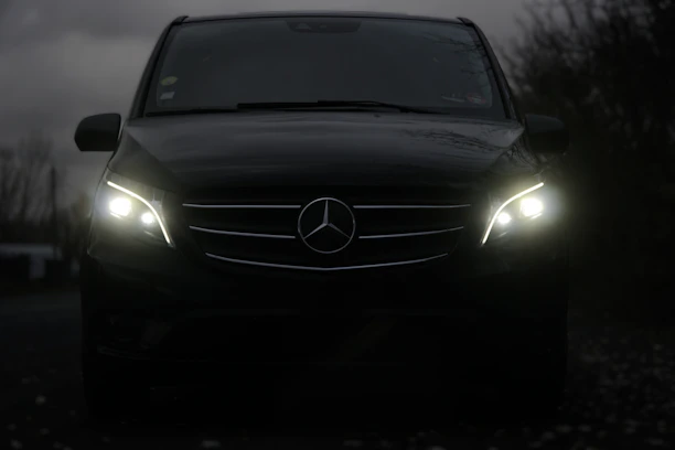 A dark mercedes van with its headlights on.