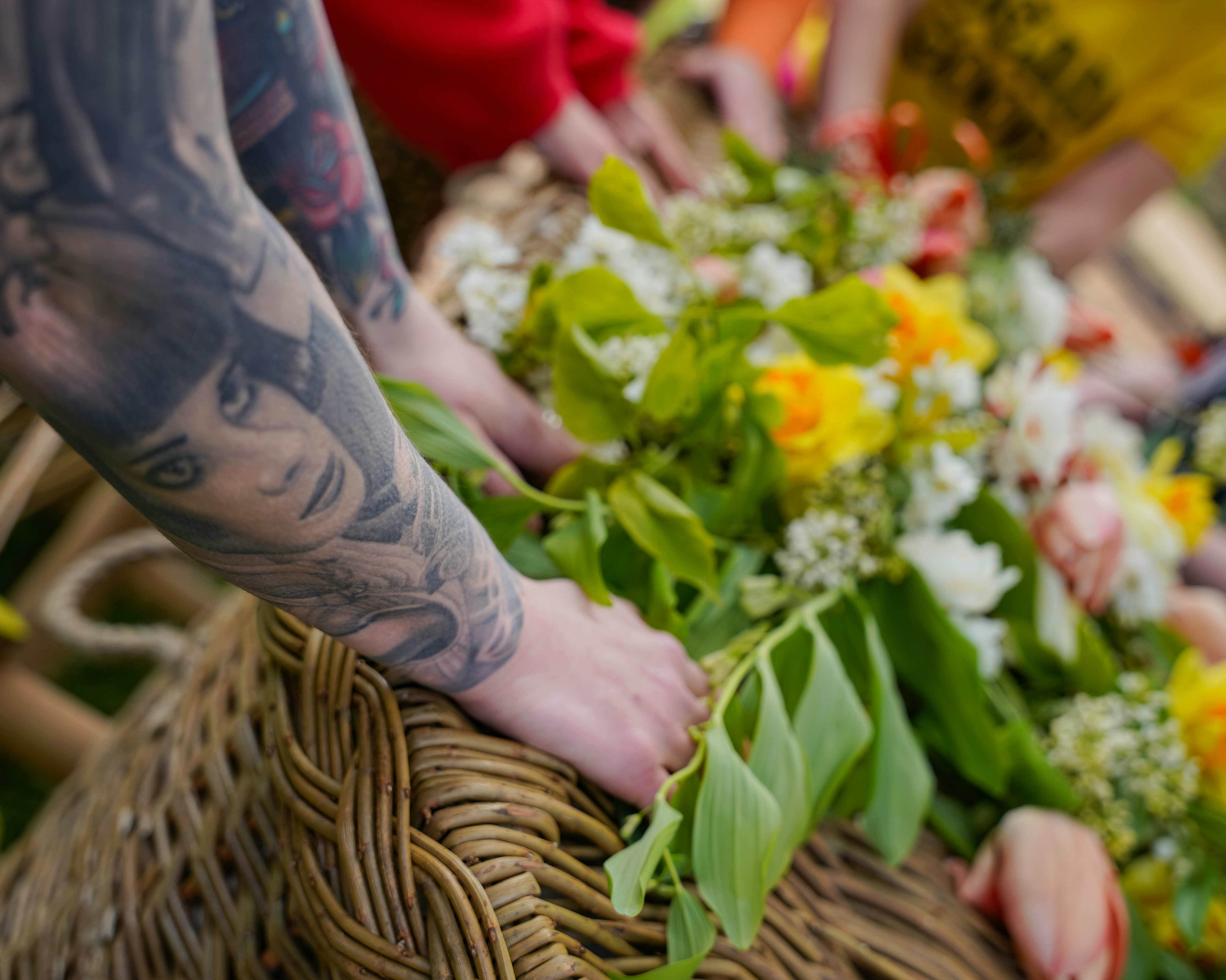 Tattooed arms arranging flowers in a basket