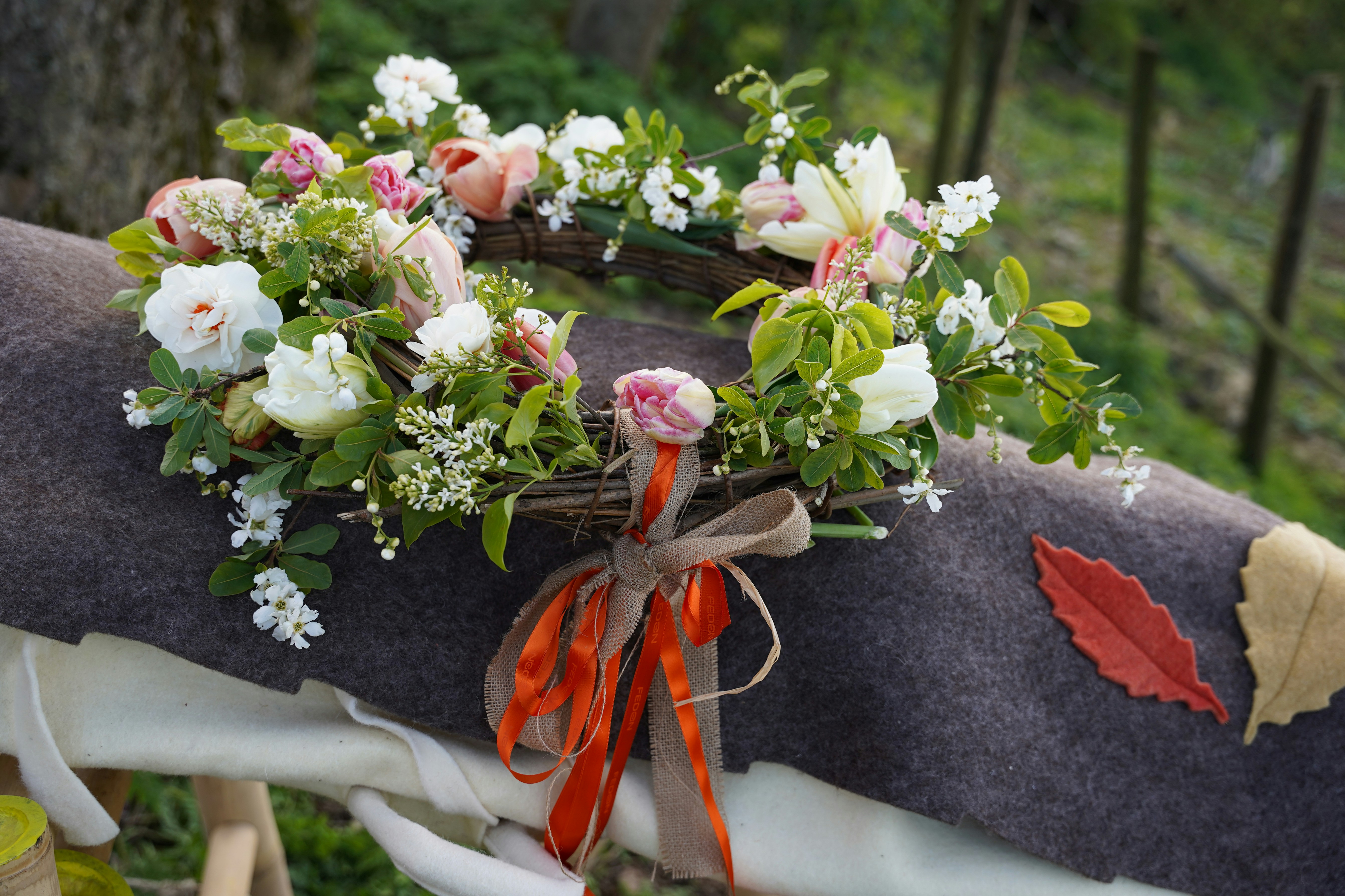 A floral wreath with ribbons rests on a textured surface.