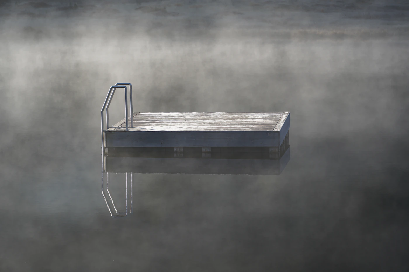 A floating wooden dock on still water, wrapped in morning mist