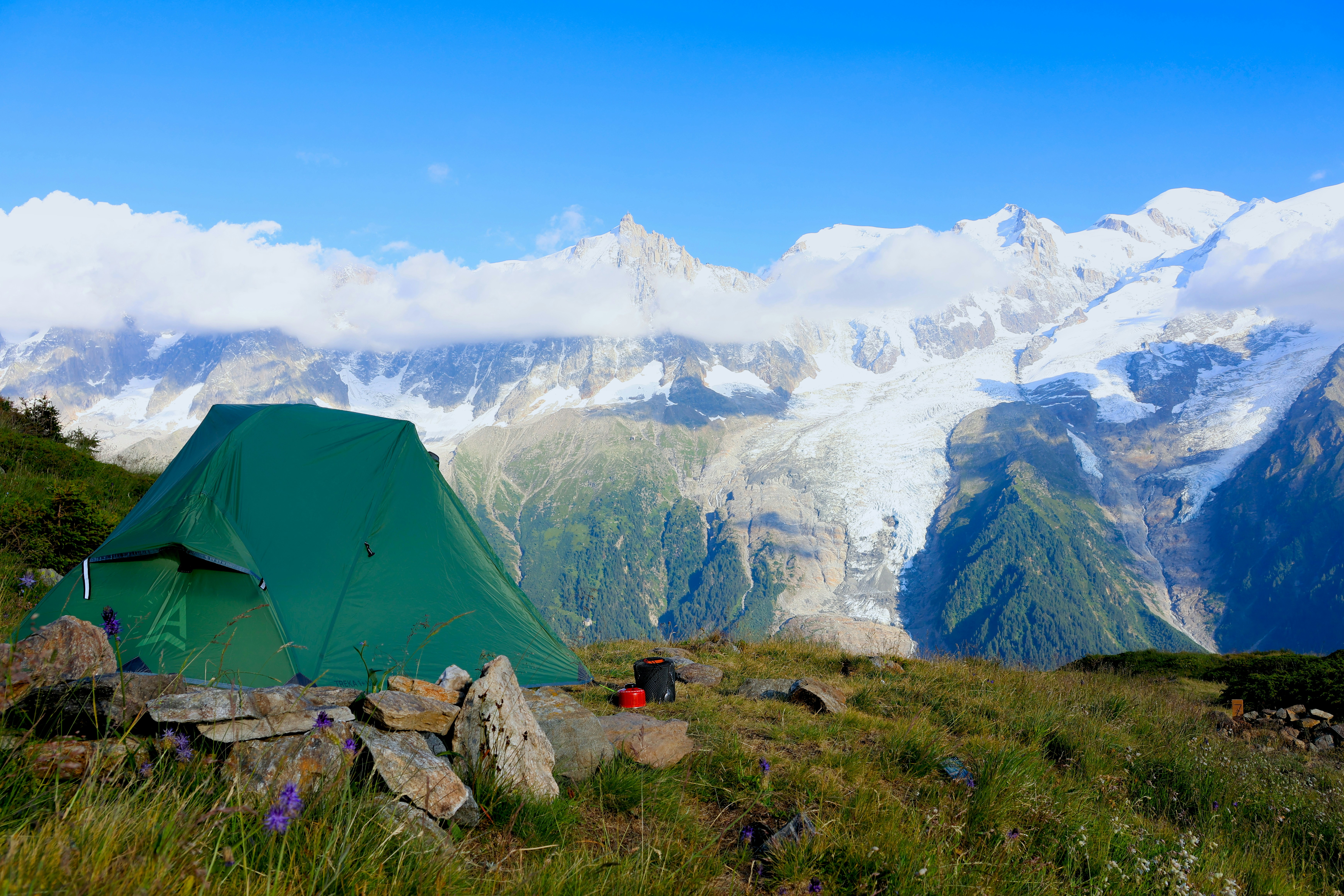 A green tent set up on a grassy mountain slope.