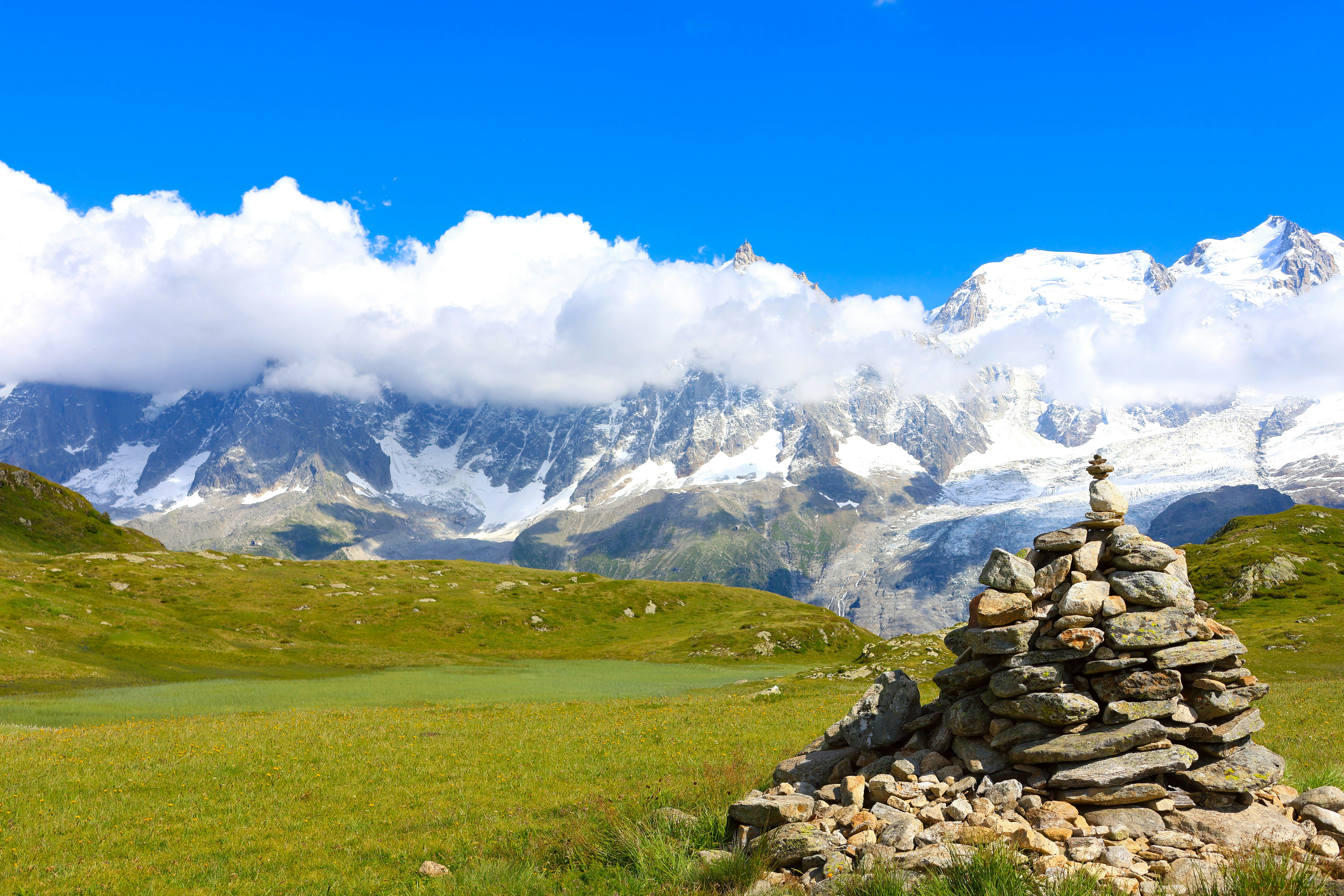 Cairn in a green meadow with snowy mountains behind
