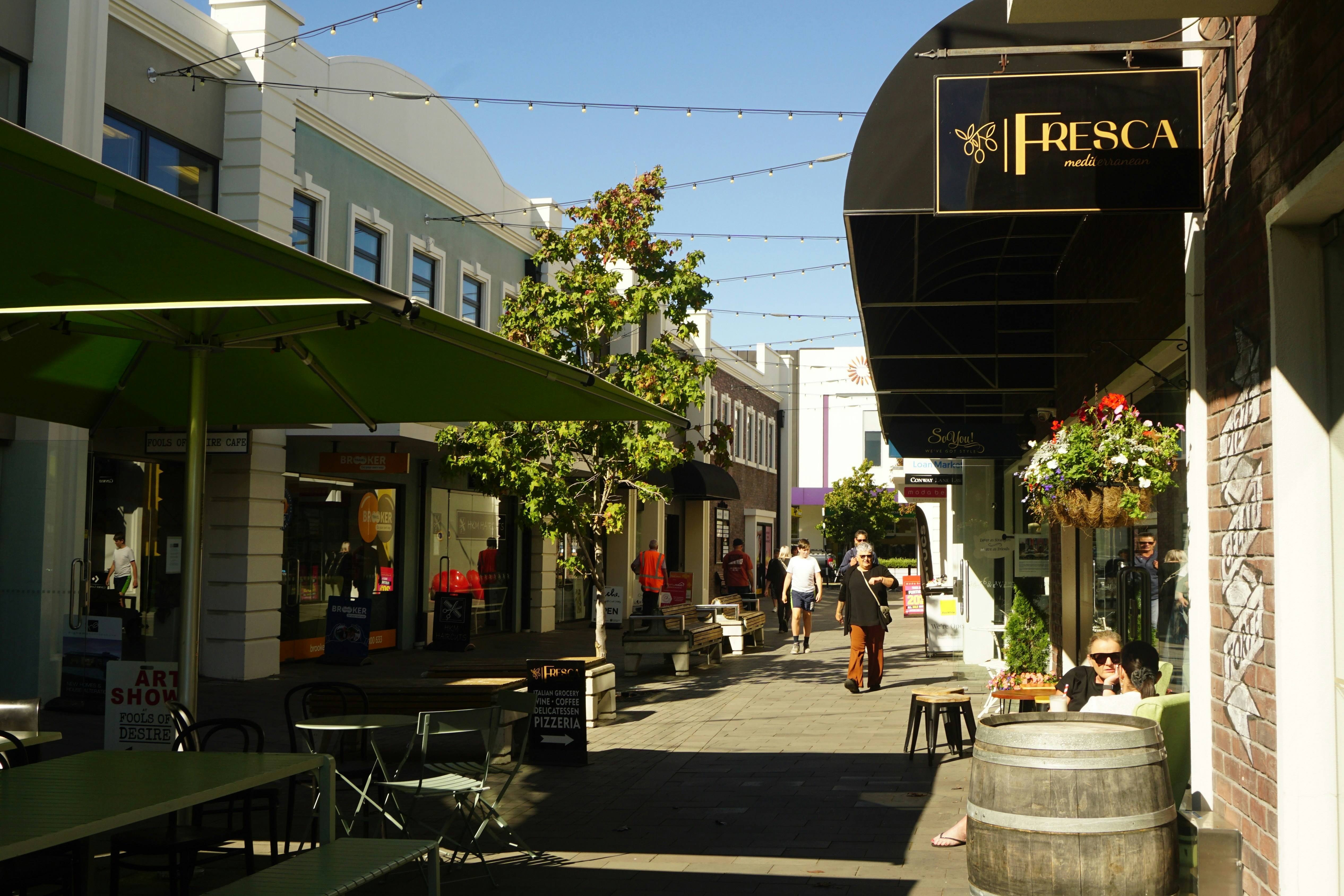 People walking down a sunny street with shops and cafes.