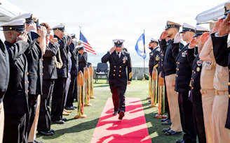 Navy officers salute during a ceremony on a sunny day.
