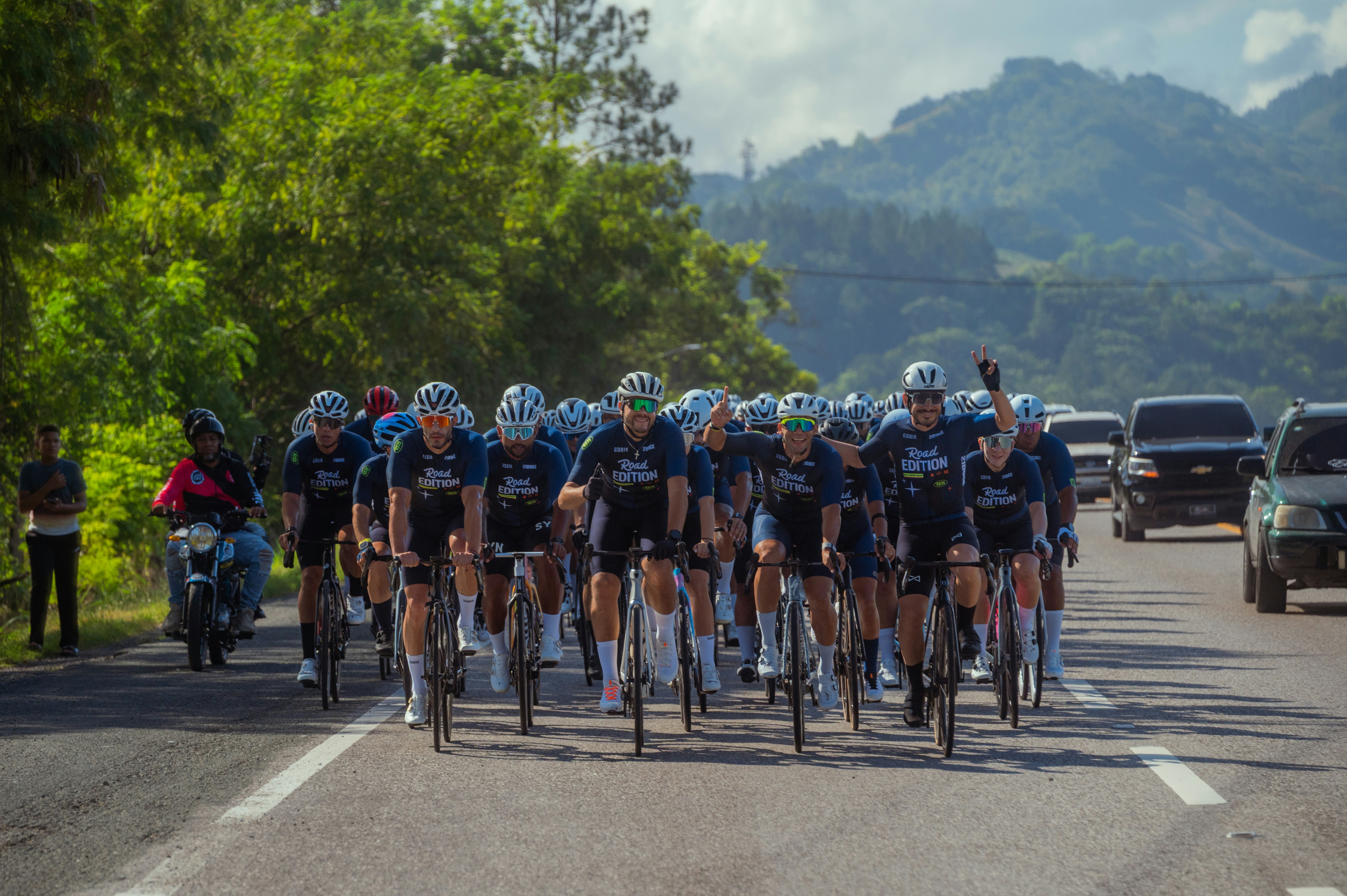 Cyclists ride together on a road with mountains