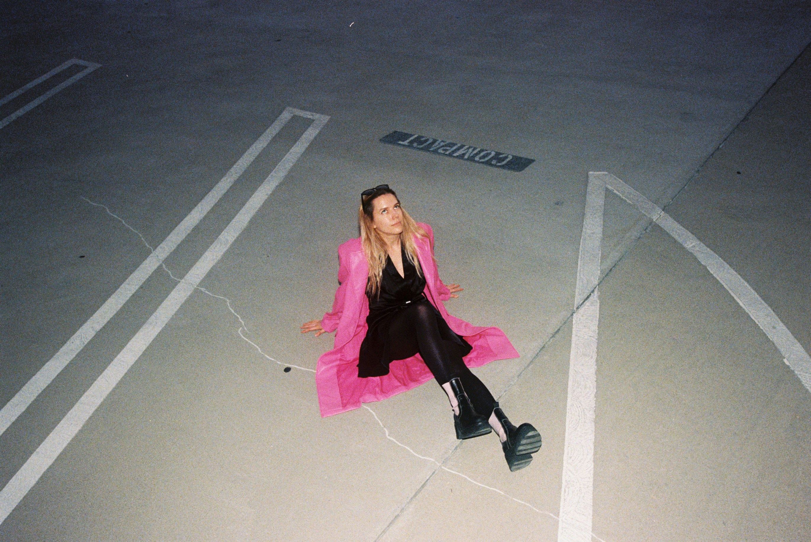 Woman in pink coat sits in empty parking lot