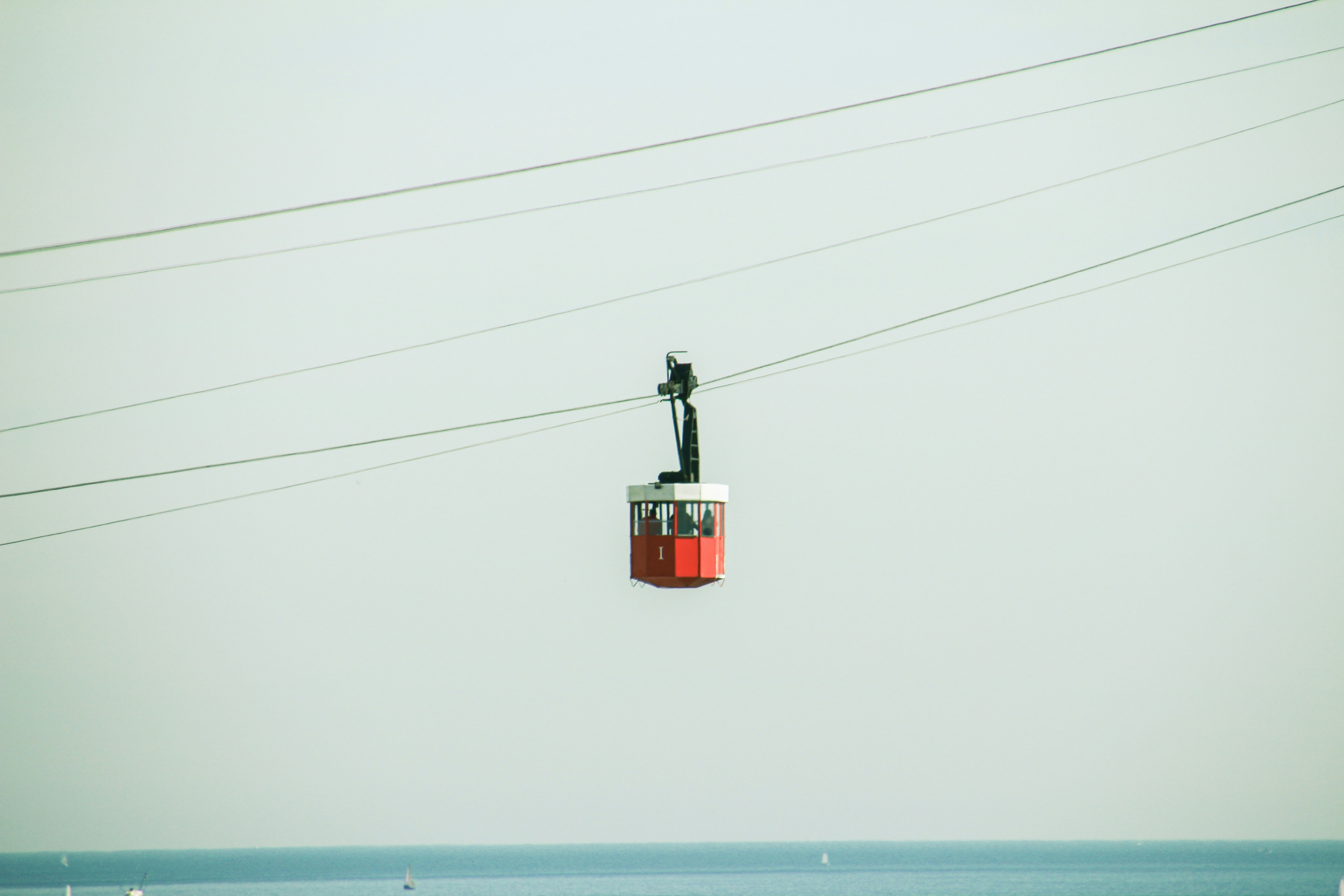 Red cable car traveling on wires over water.