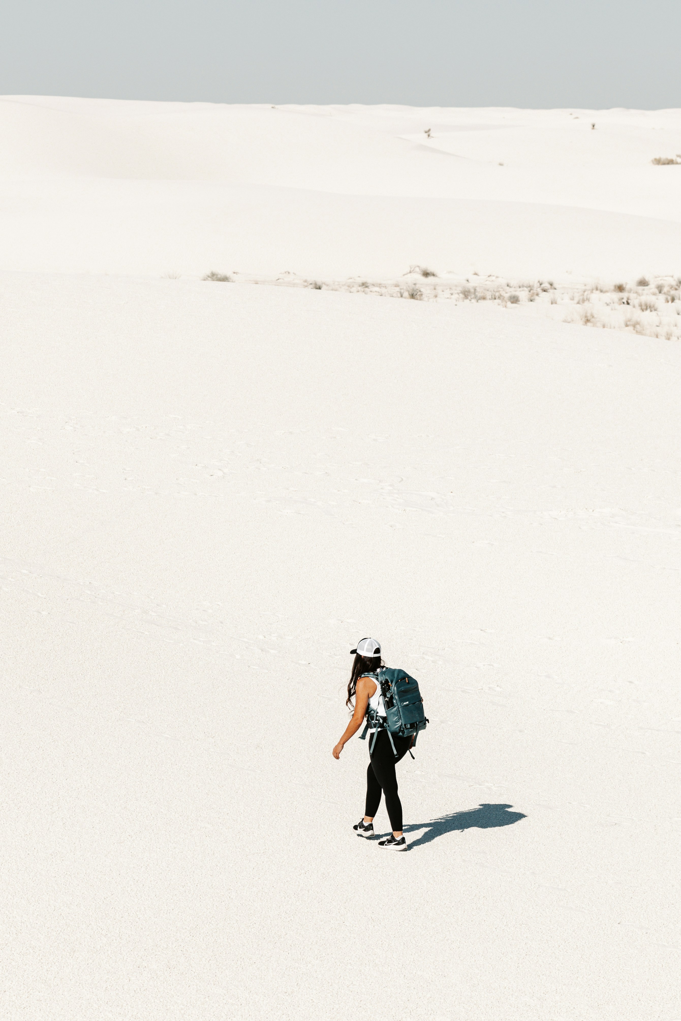 Woman with backpack walking across vast white desert landscape.