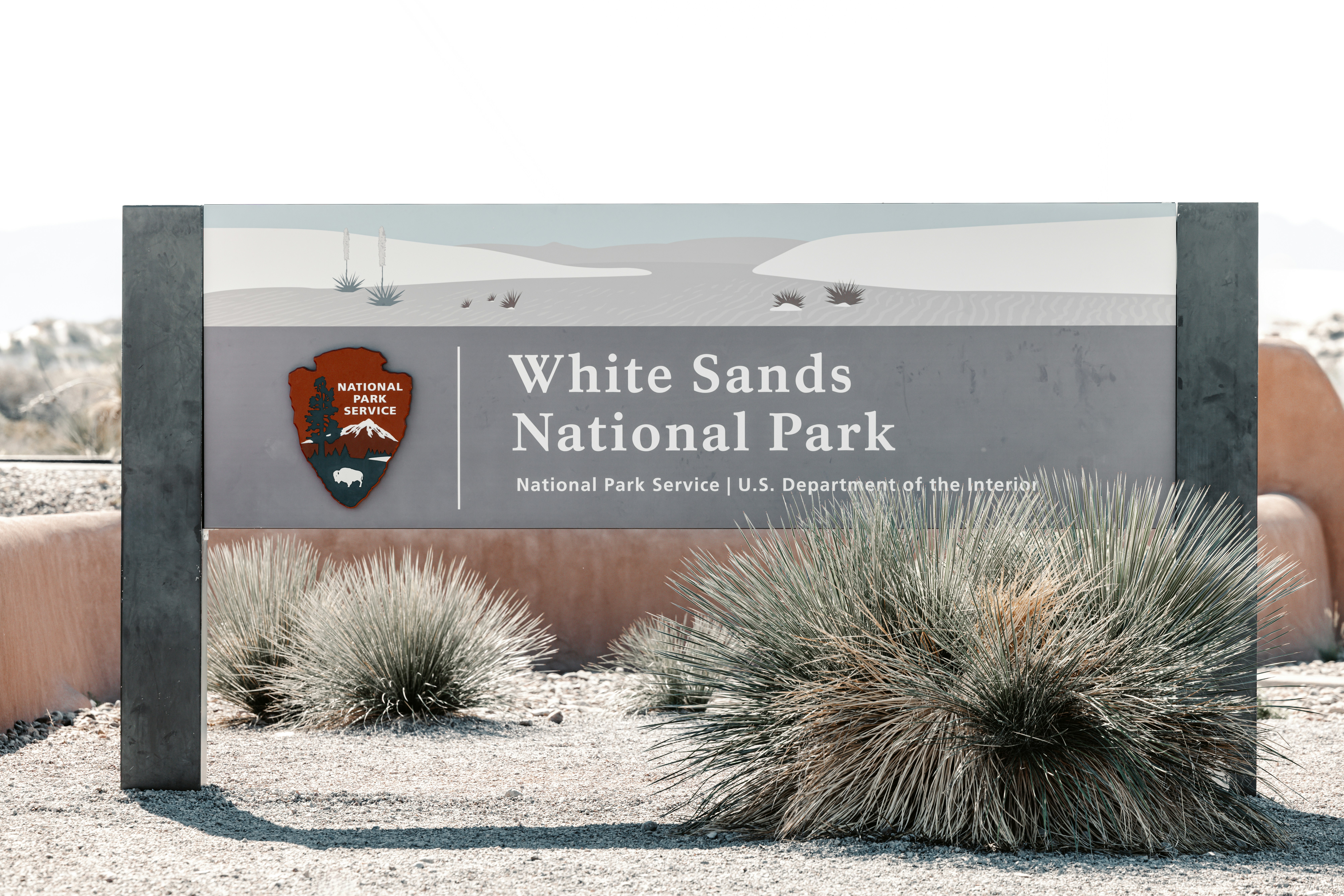 White sands national park entrance sign with desert plants.