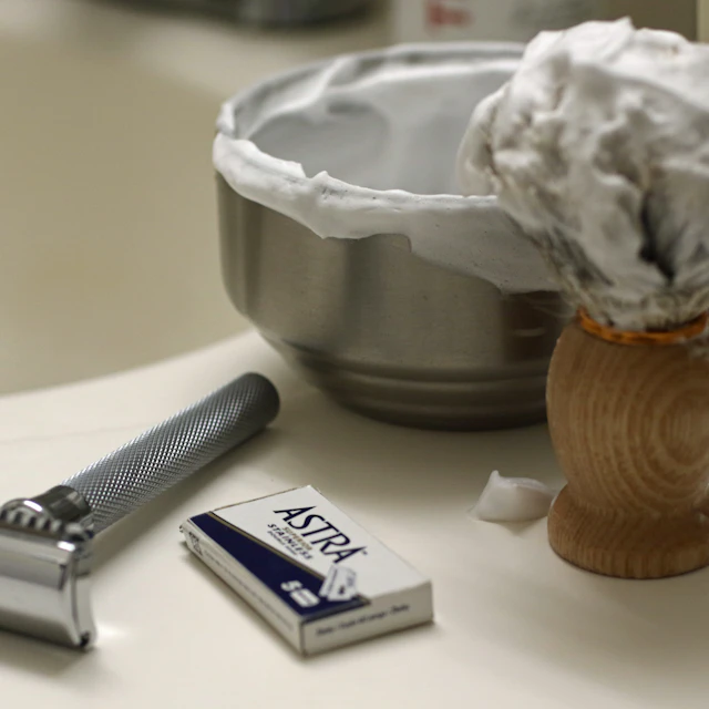 A double-edge safety razor arranged with a tub of shaving cream and a shaving brush