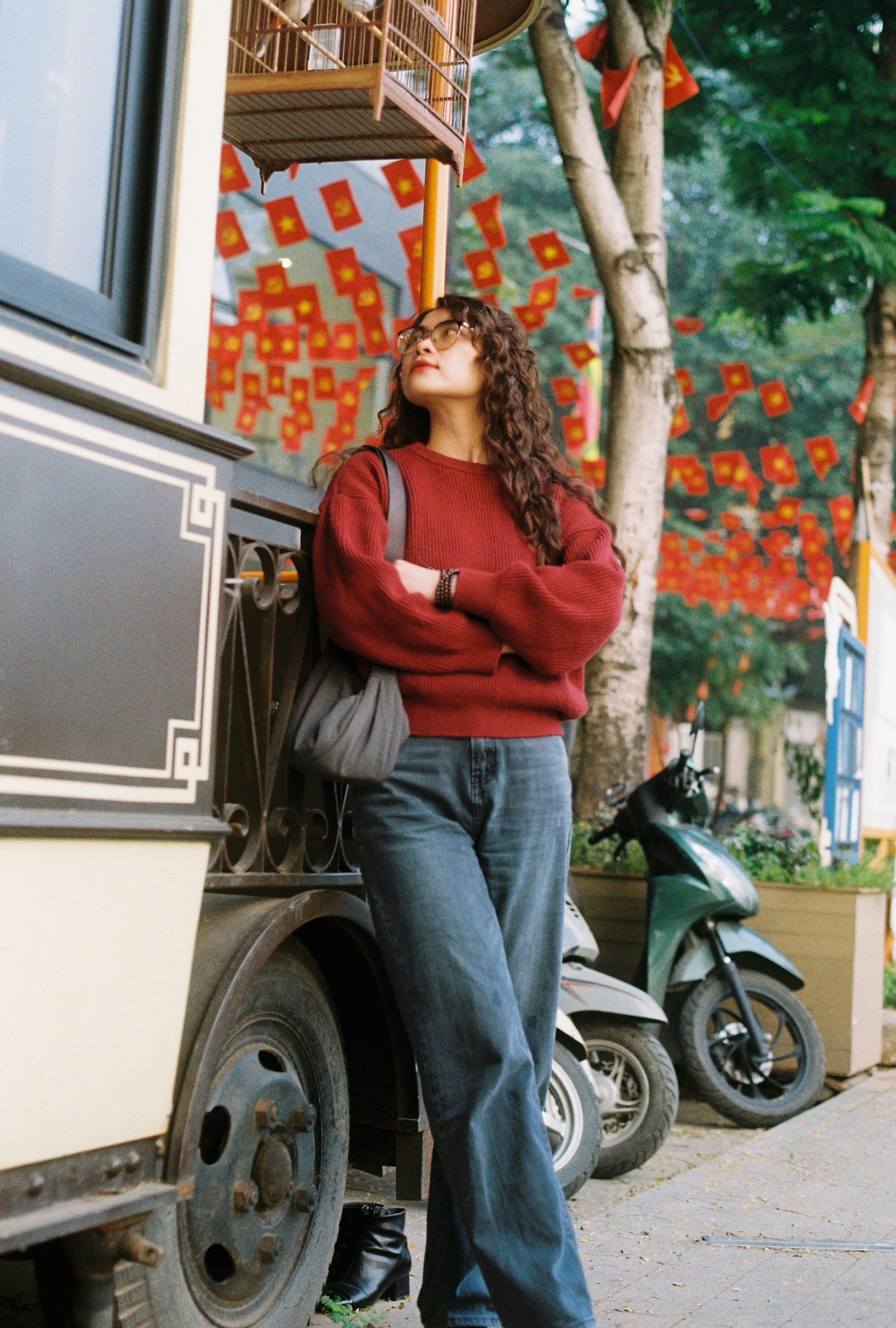 Woman in red sweater and jeans stands by vehicle.