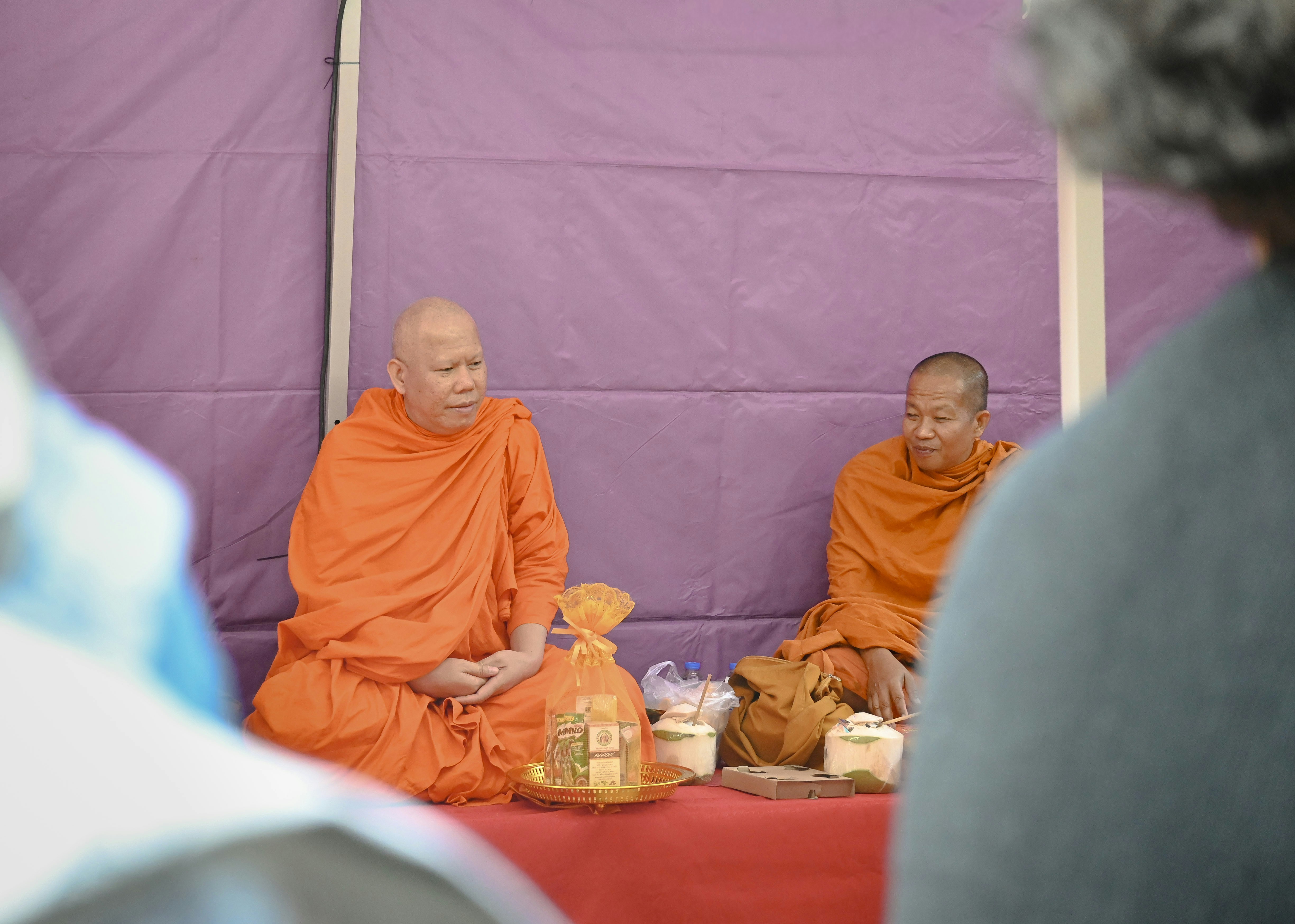 Two buddhist monks in orange robes sit indoors.