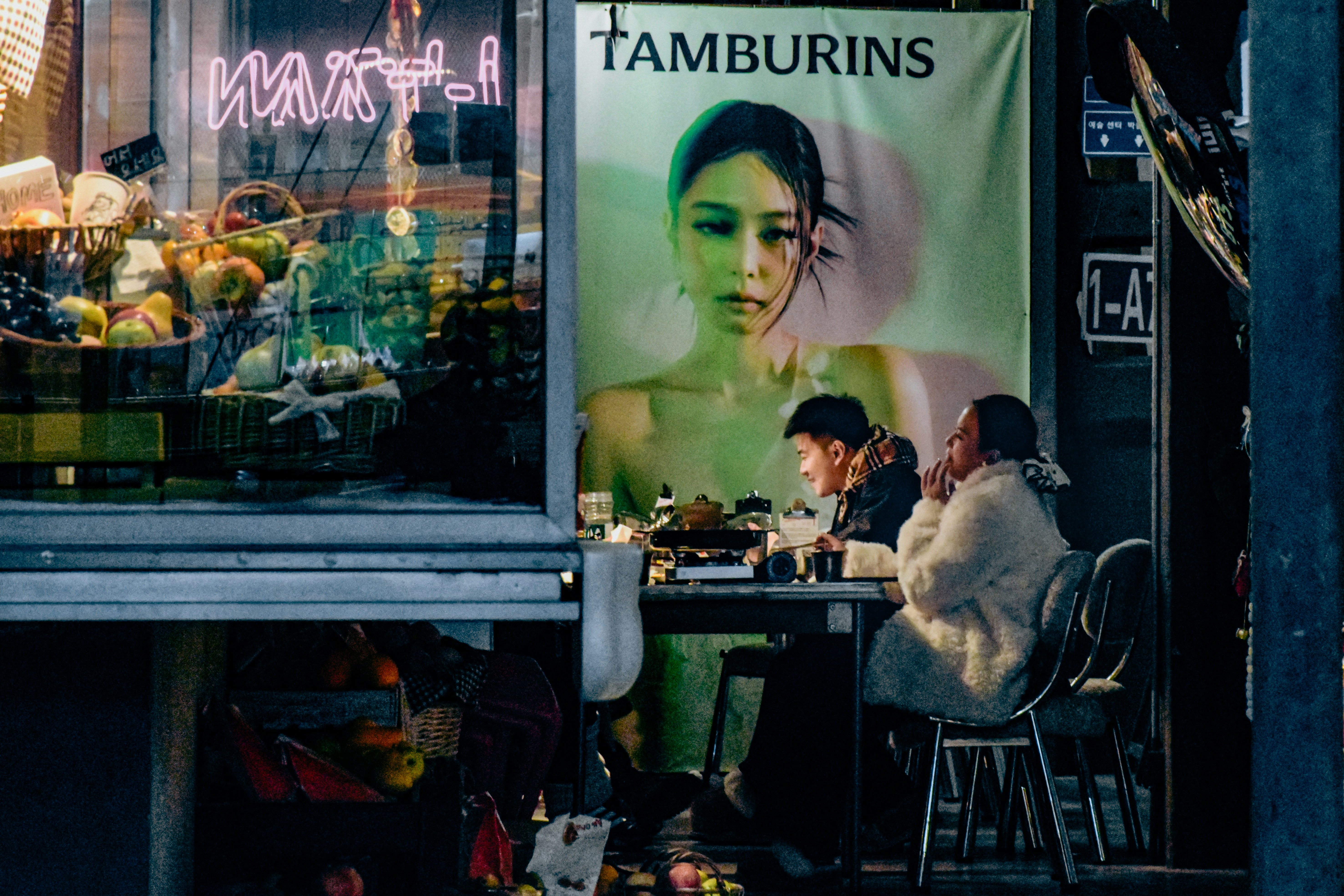 People sit at a table outside a shop with advertisement.