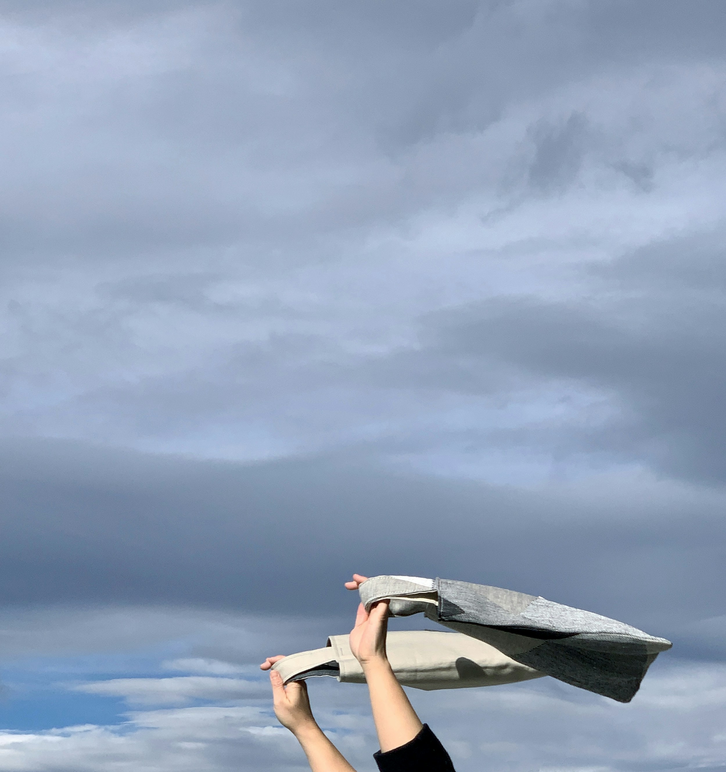 Hands hold folded fabric against cloudy sky