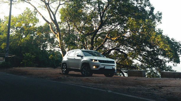 Silver suv parked on a dirt road near trees.