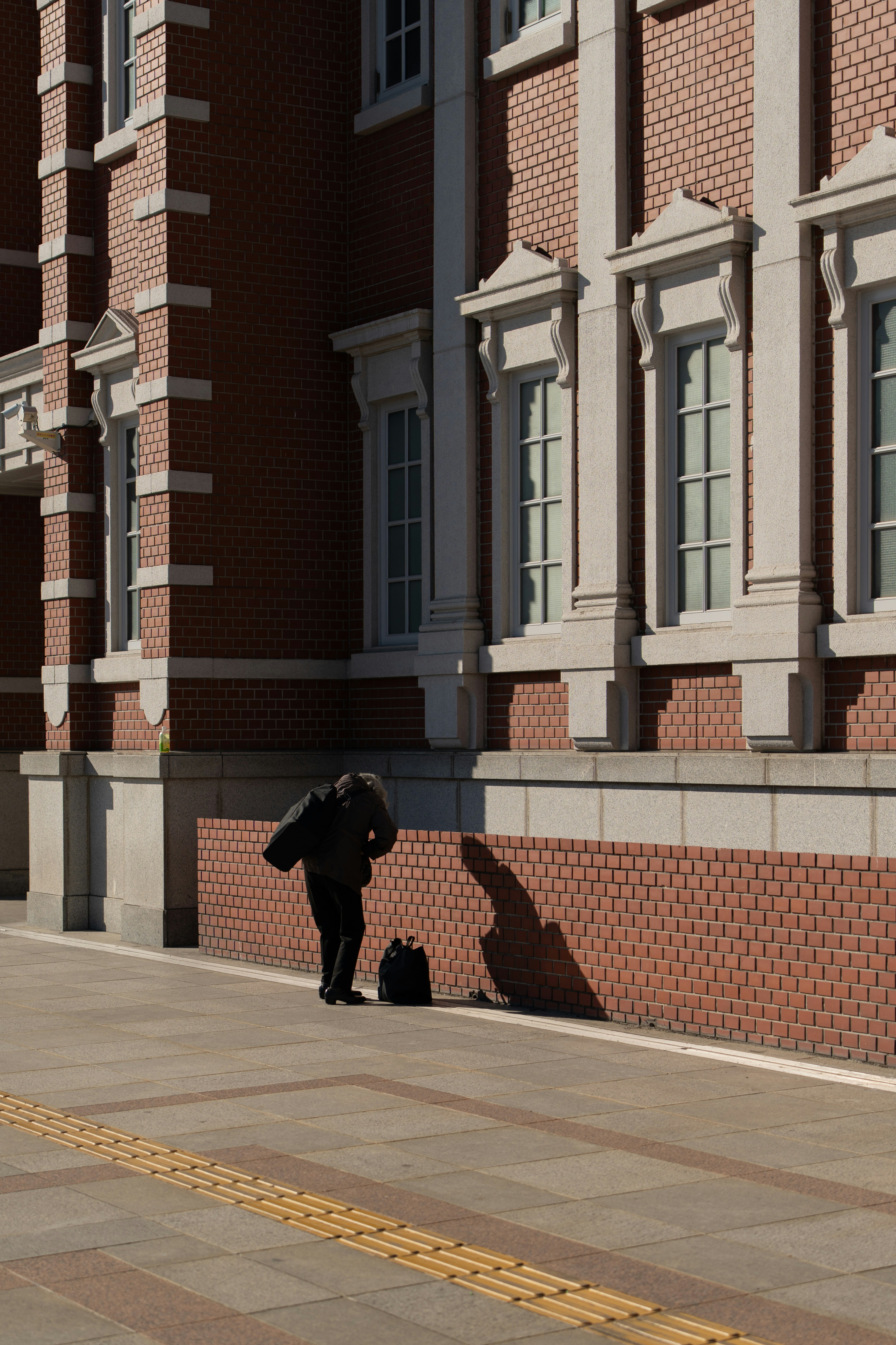 벽돌 건물 옆을 배낭을 메고 그림자를 바라보는 남자