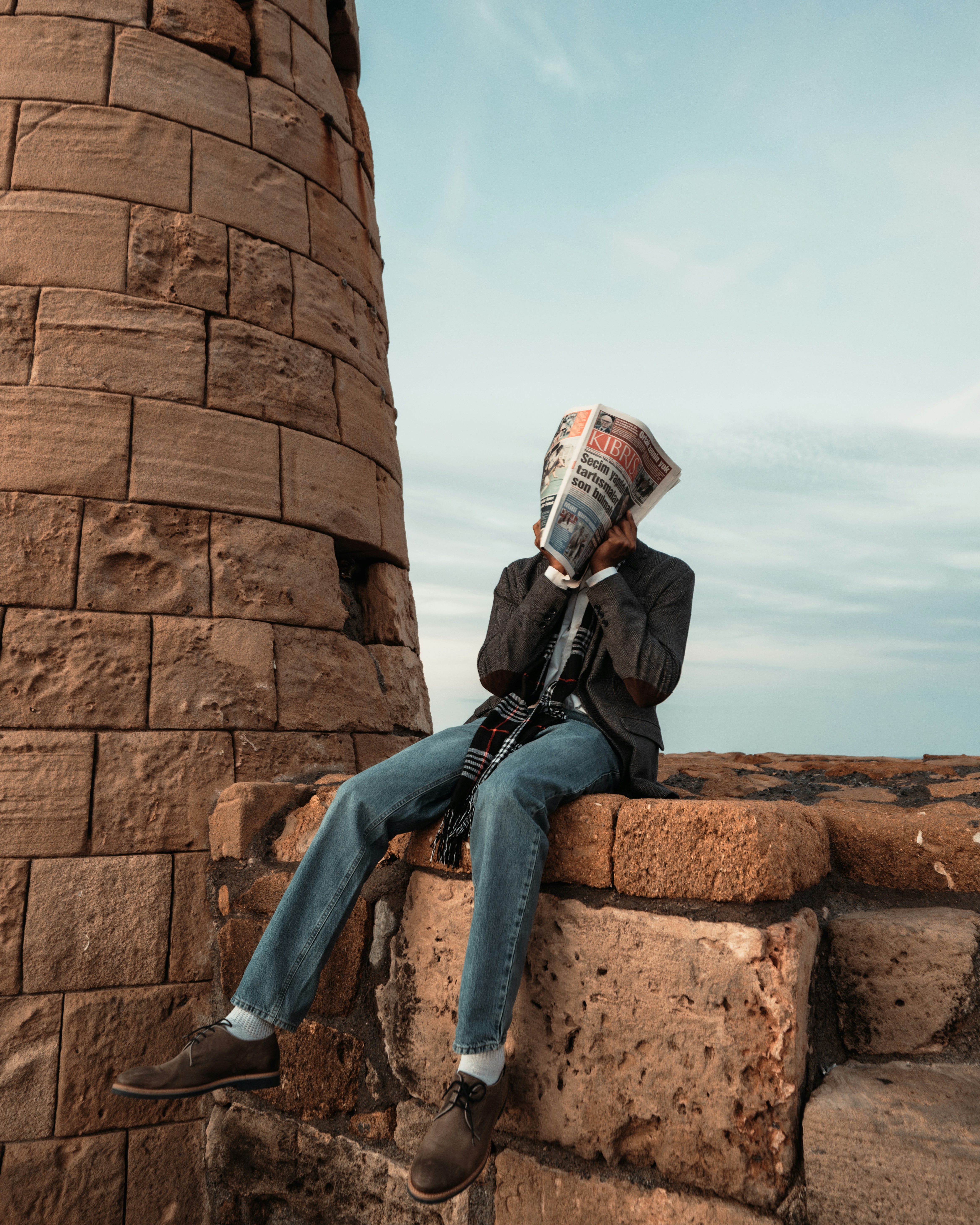 Persona sentada en una pared de piedra leyendo el periódico
