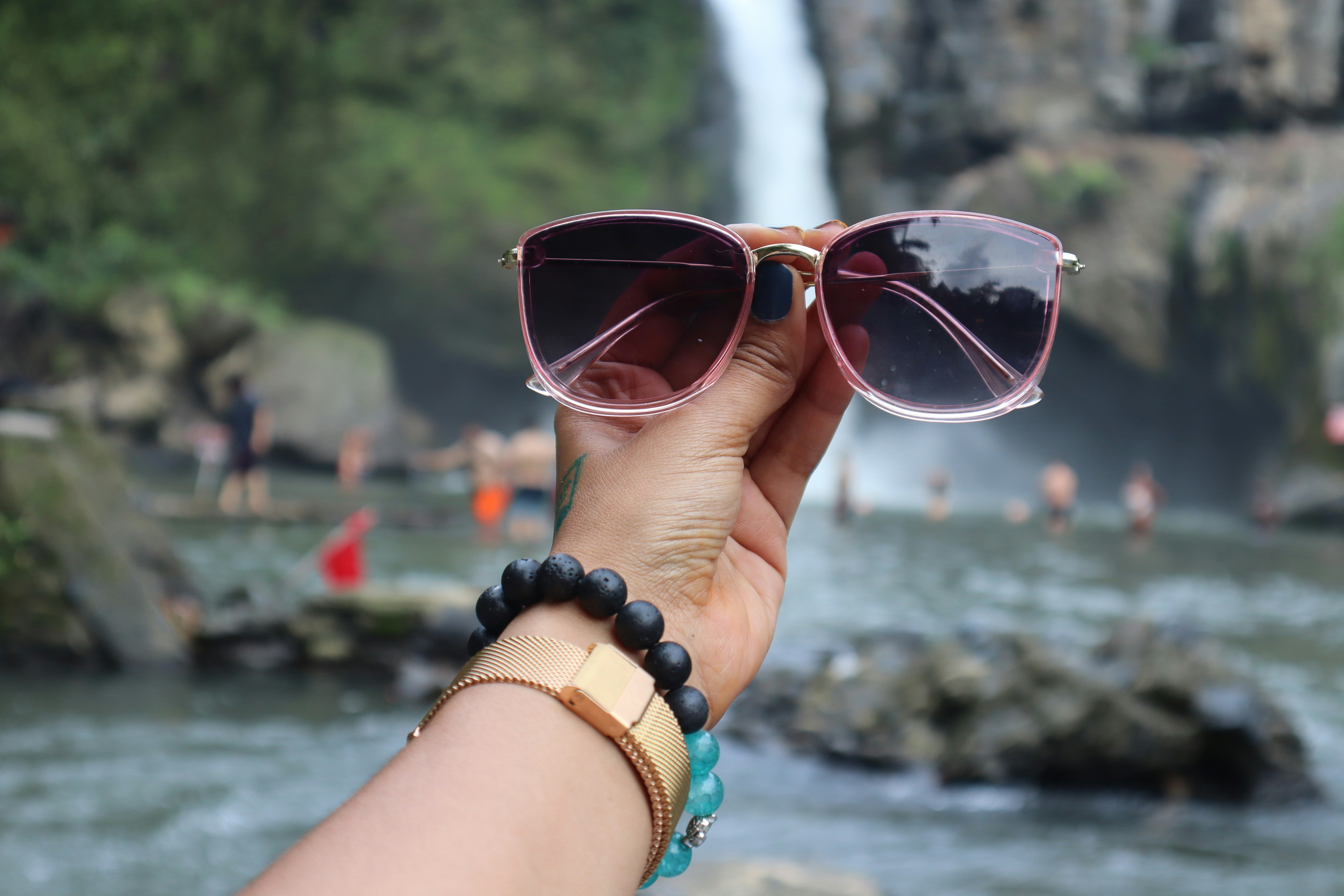Hand holding sunglasses with waterfall background