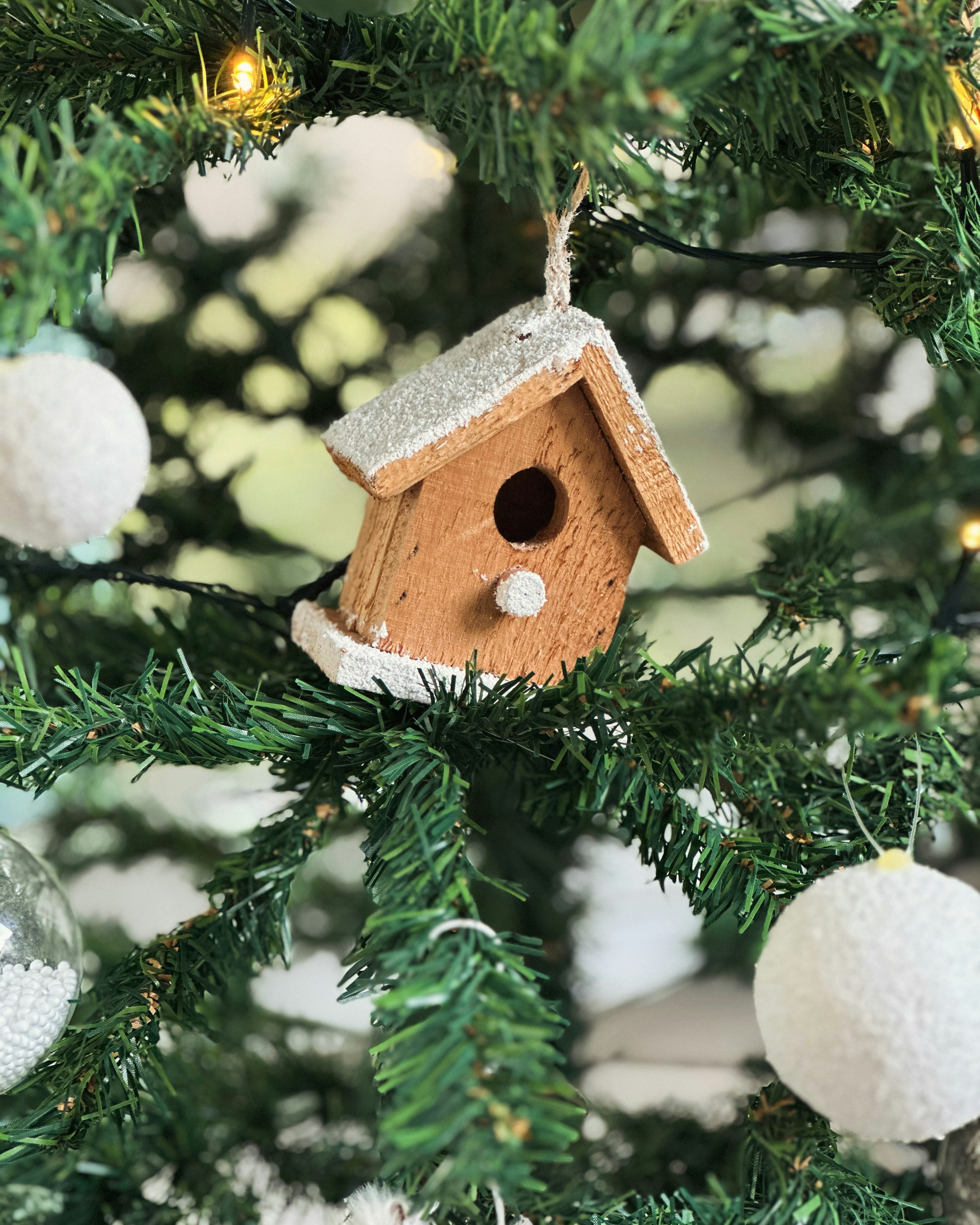 Ein kleines hölzernes Vogelhaus-Ornament hängt an einem Weihnachtsbaum.