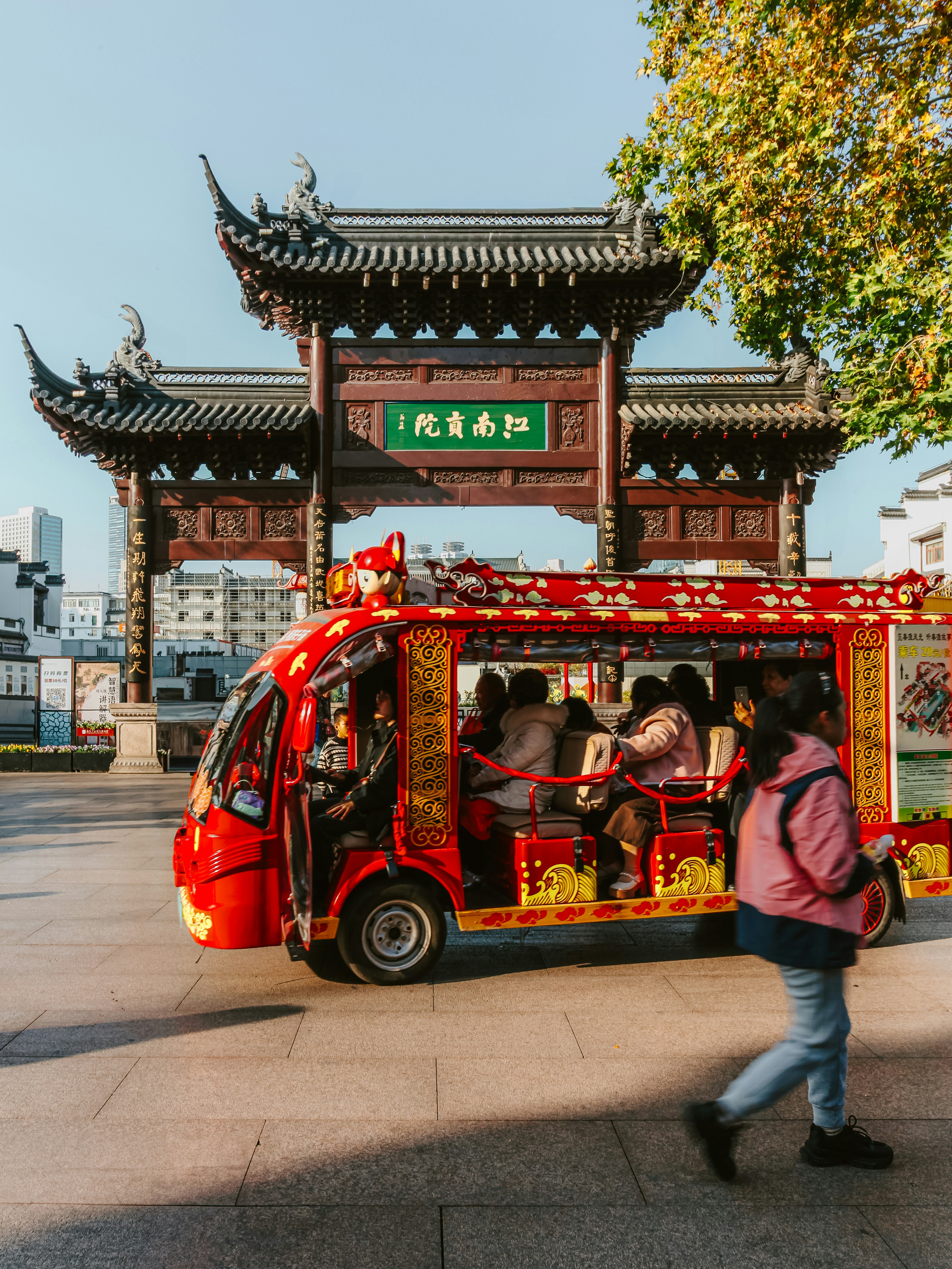 A red tourist vehicle passes a traditional chinese gate.