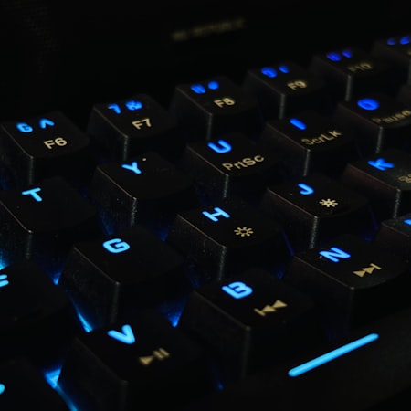 Close-up of a backlit mechanical keyboard with blue illumination showing individual keycaps