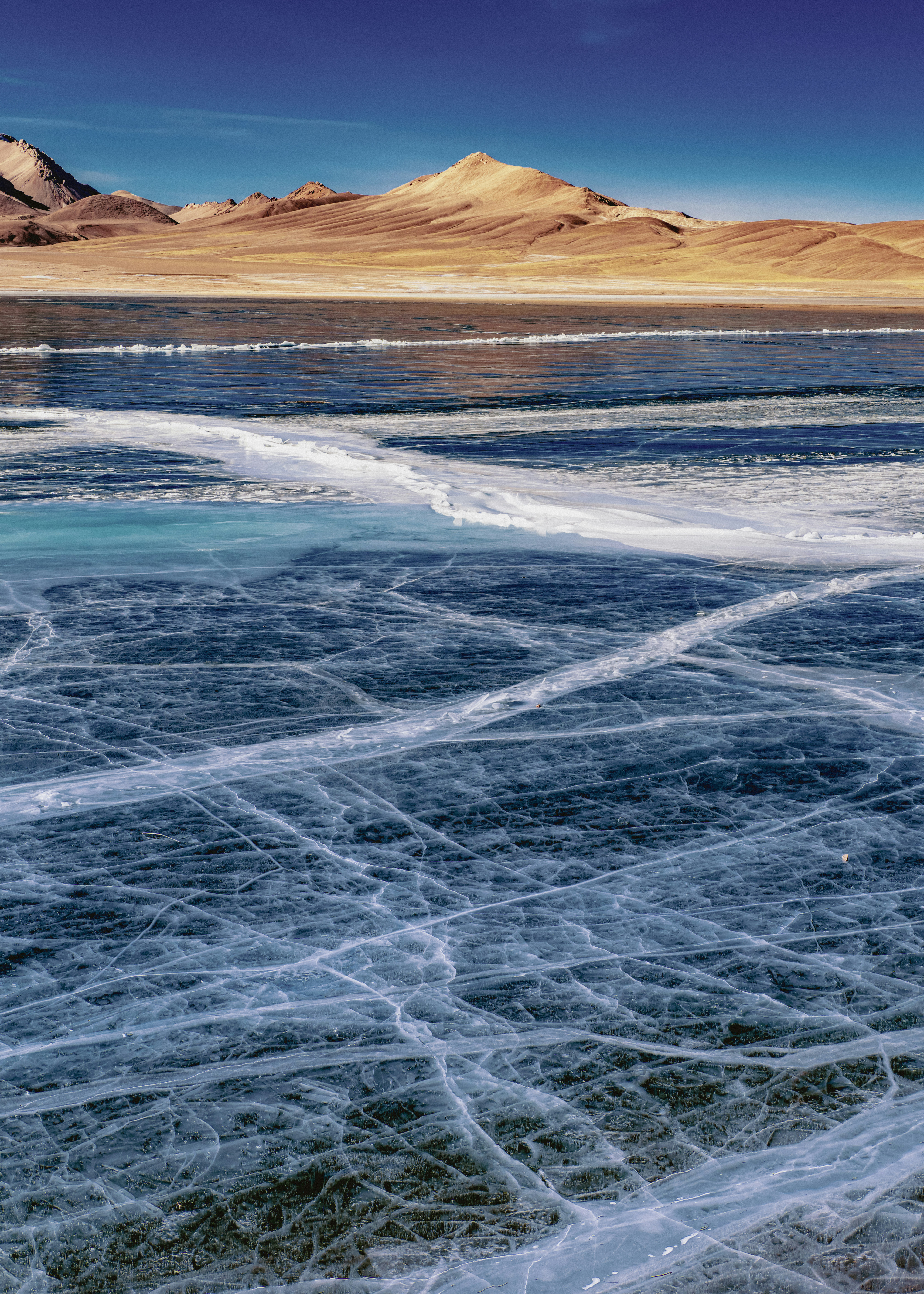 Cracked ice on a frozen lake with mountains beyond.