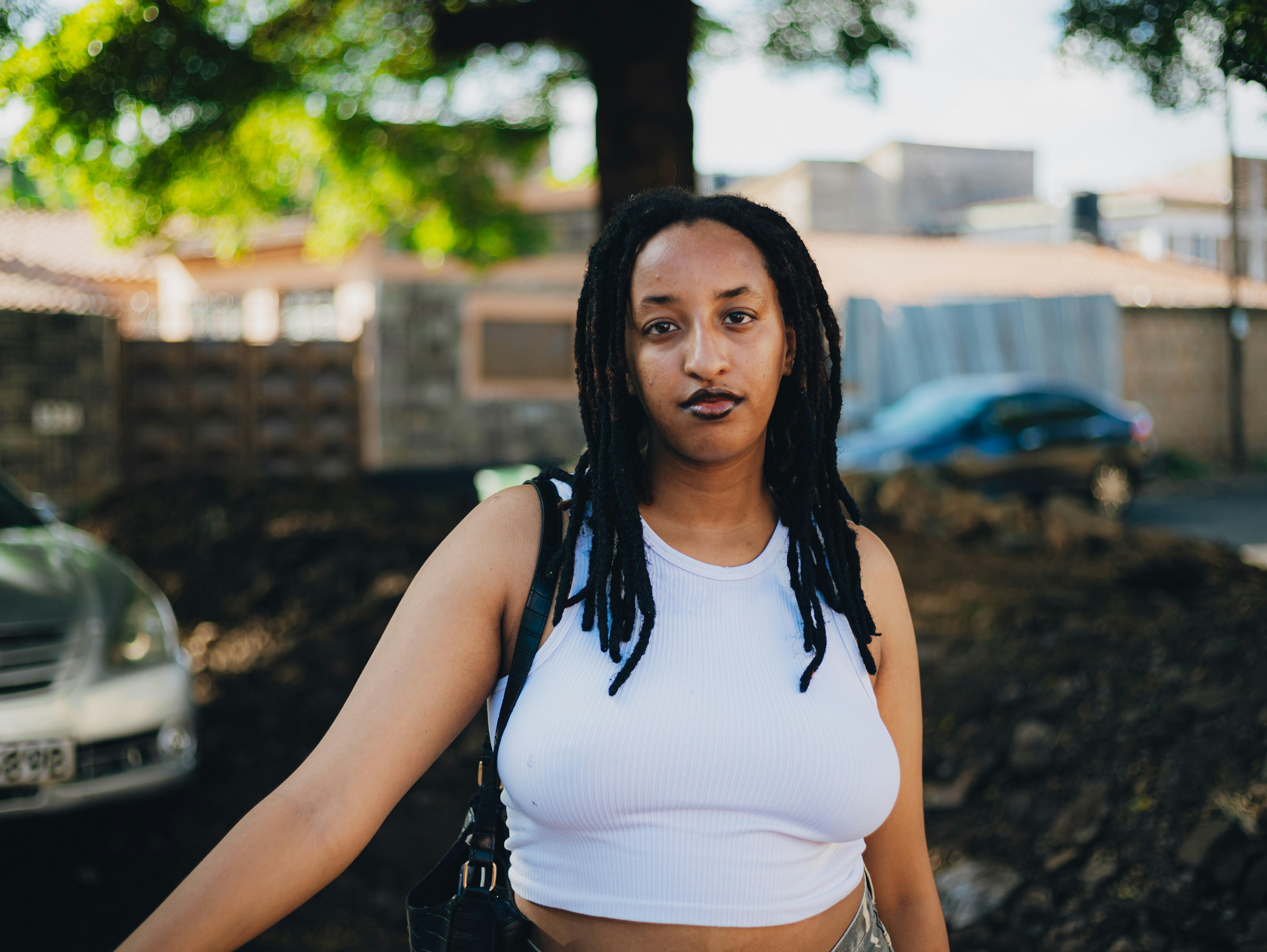 A young woman with dreadlocks wearing a white crop top.