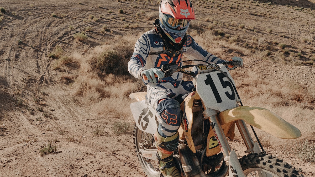 Motocross rider on a yellow dirt bike in a desert trail landscape