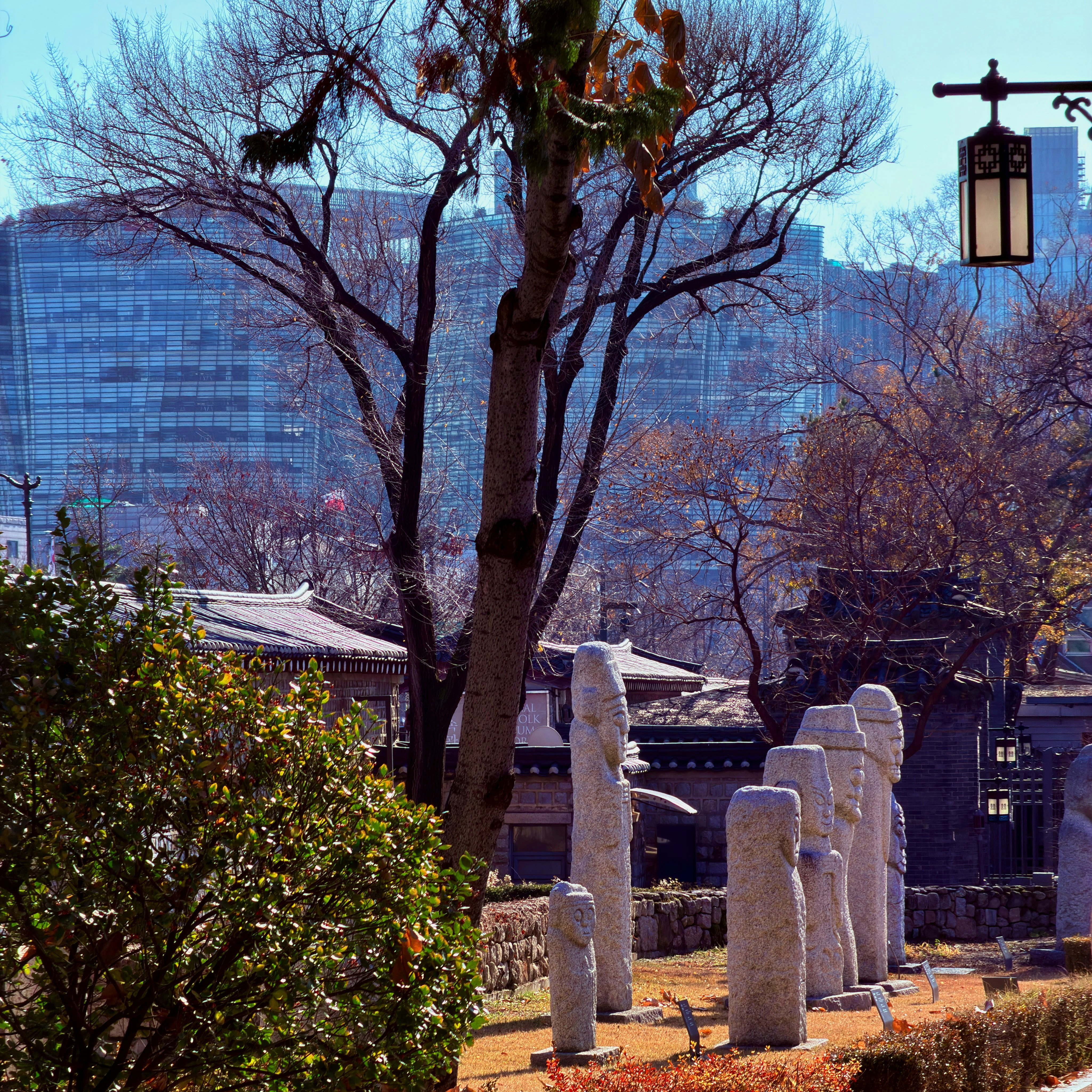 Stone statues stand in a park with buildings behind.