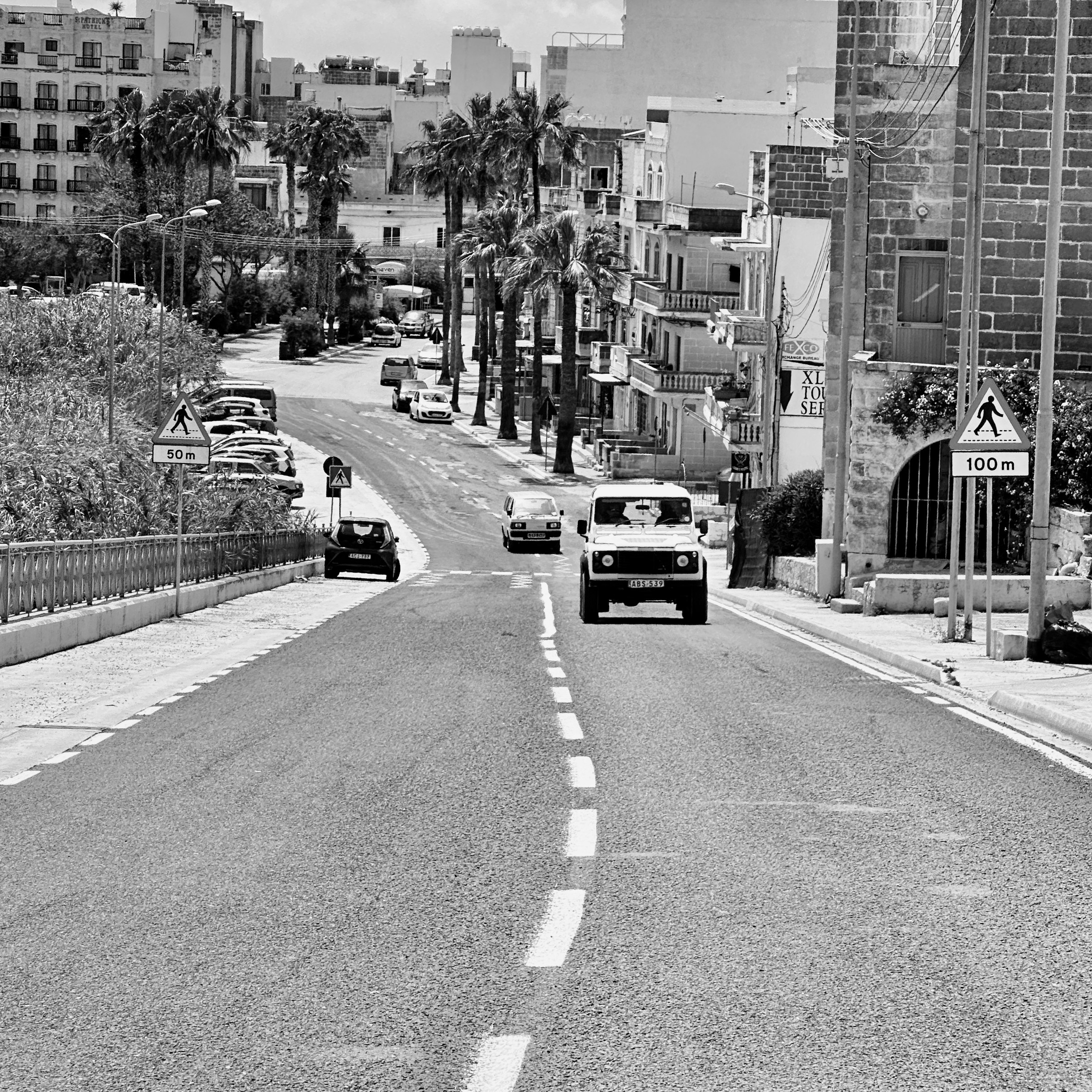Cars driving on a road with buildings and palm trees.