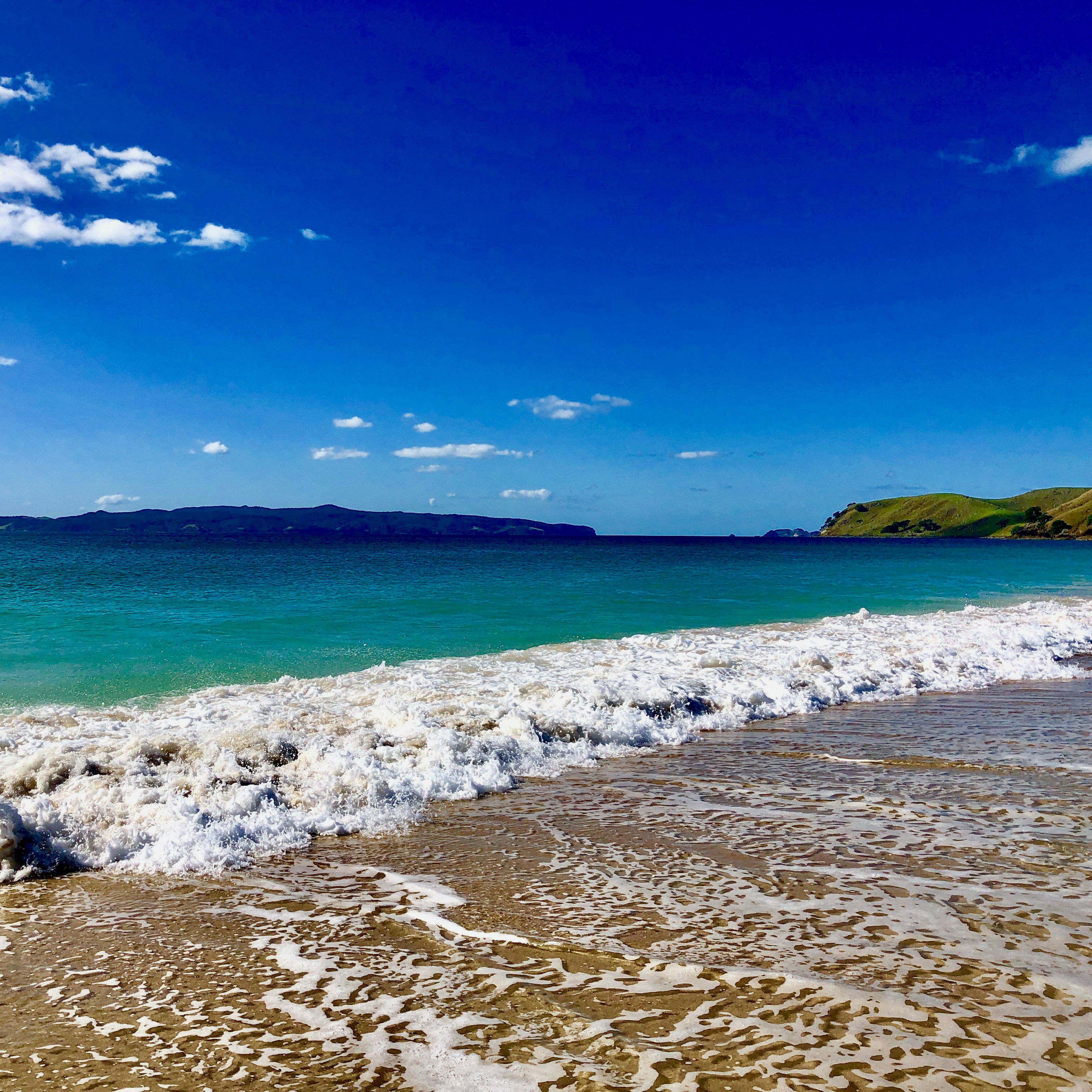 Waves crashing on a sandy beach under blue sky