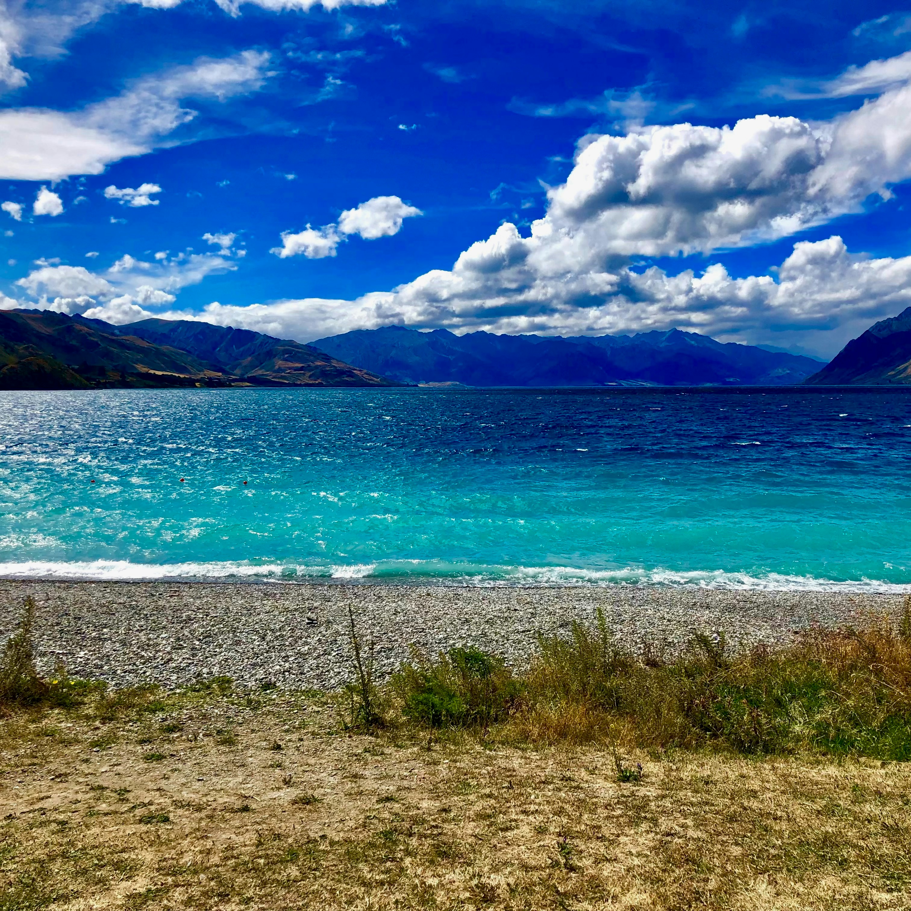 Turquoise lake waters with mountains under a cloudy sky.
