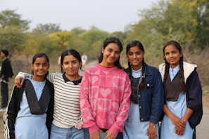 Five smiling girls stand together outdoors.